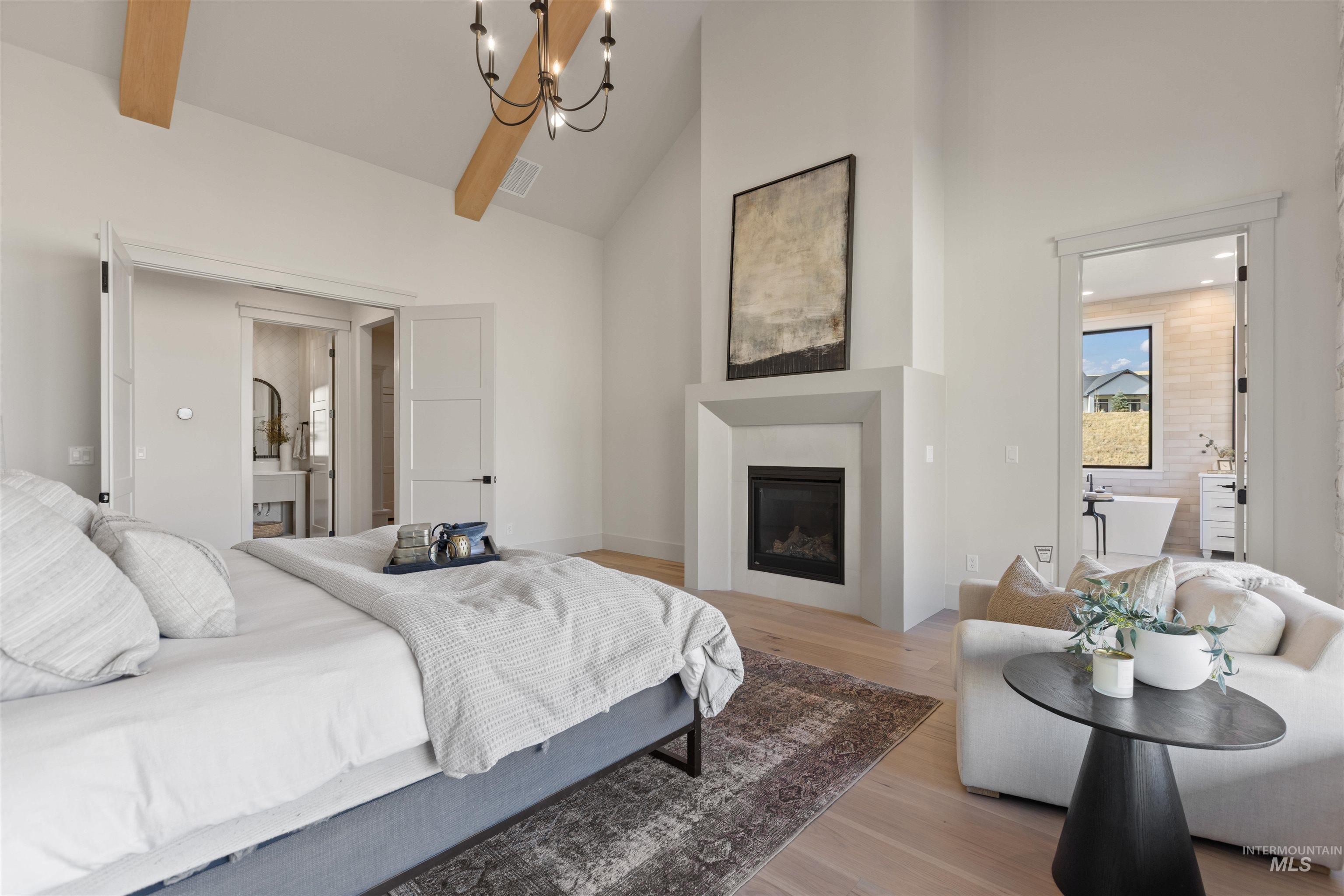 Bedroom with high vaulted ceiling, wood finished floors, a glass covered fireplace, a chandelier, and connected bathroom