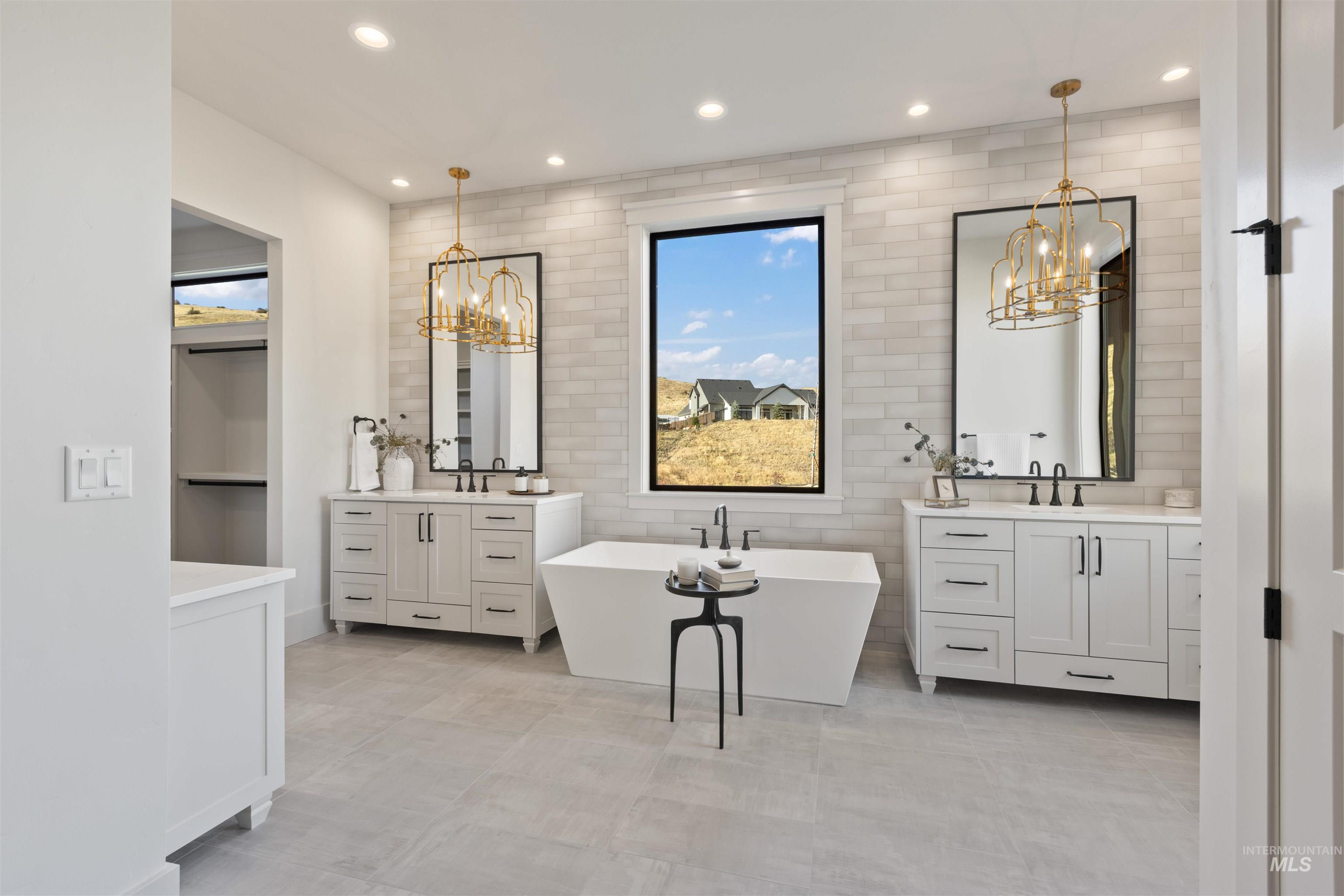 Full bathroom featuring a chandelier, two vanities, recessed lighting, a freestanding tub, and light tile patterned flooring