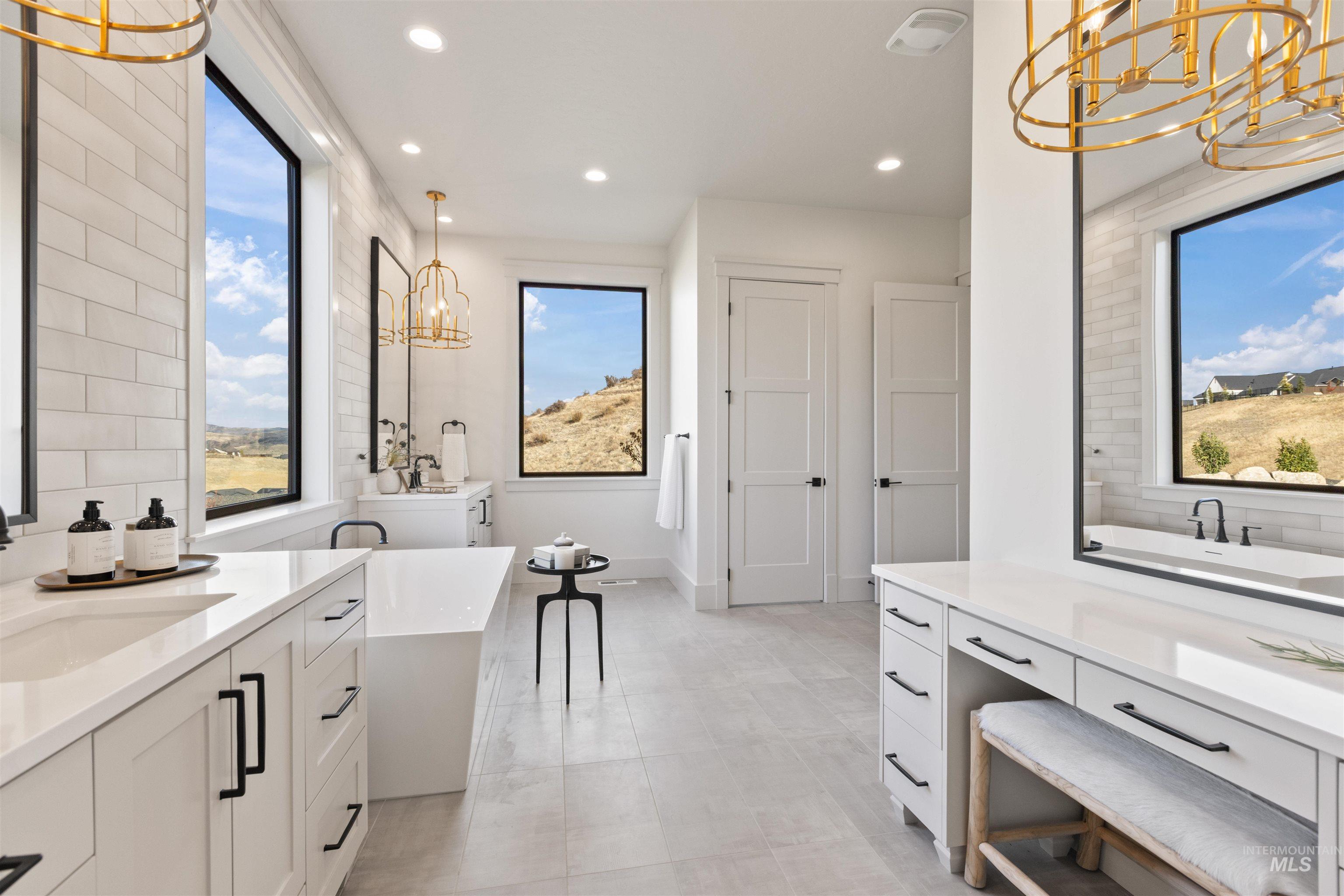 Bathroom featuring a chandelier, a freestanding tub, two vanities, backsplash, and recessed lighting