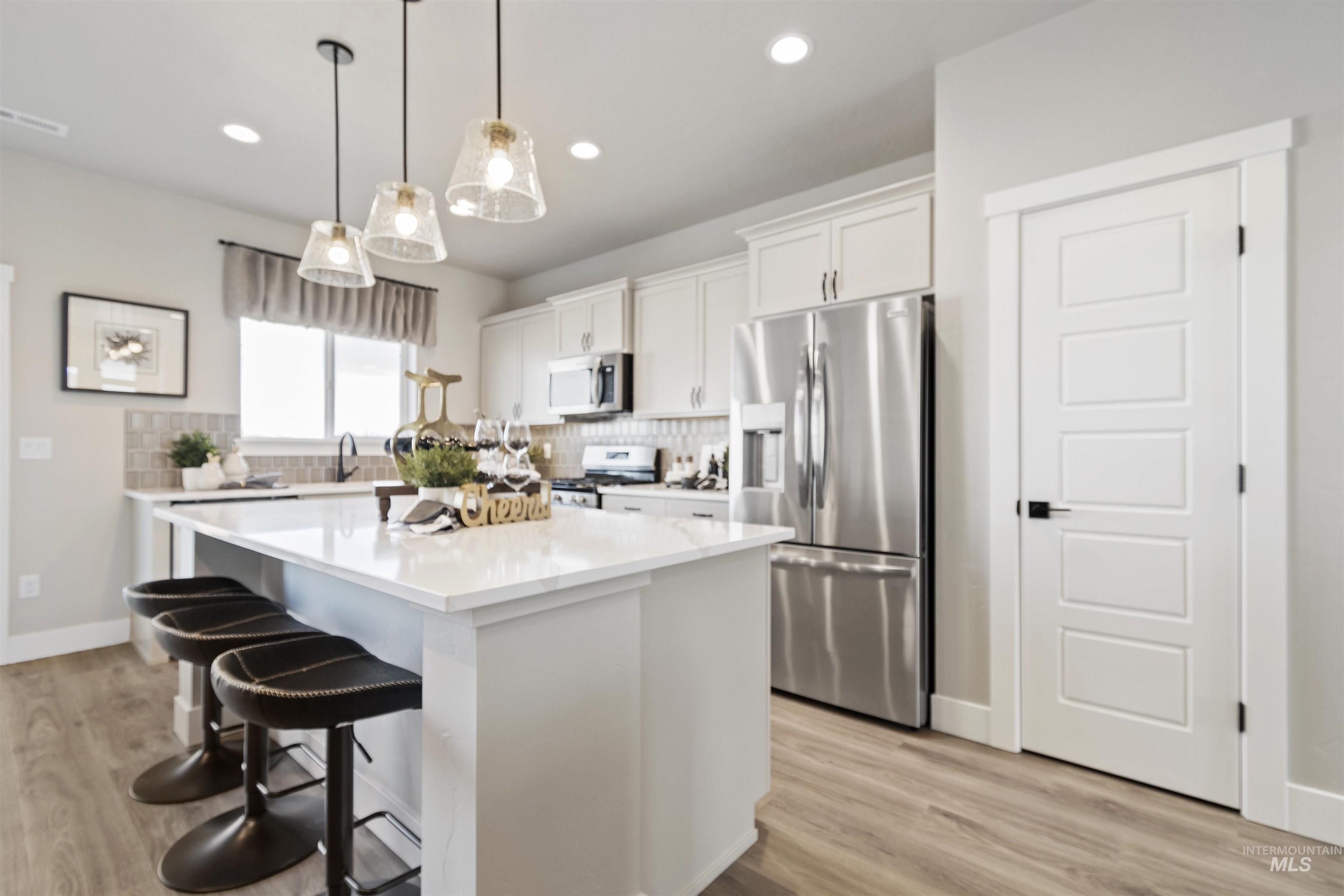 Kitchen with appliances with stainless steel finishes, white cabinets, pendant lighting, a breakfast bar, and decorative backsplash