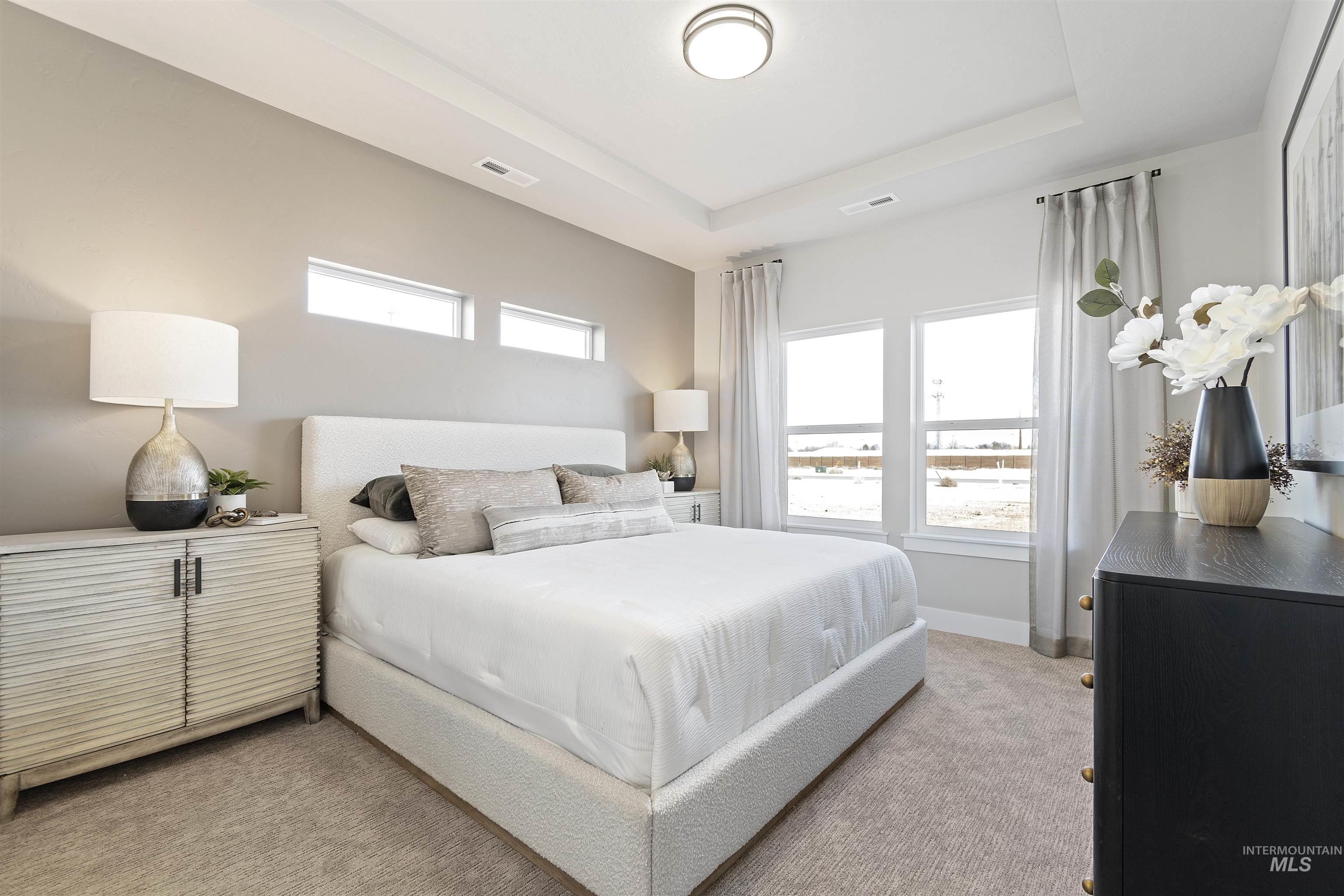 Bedroom with a raised ceiling and light colored carpet