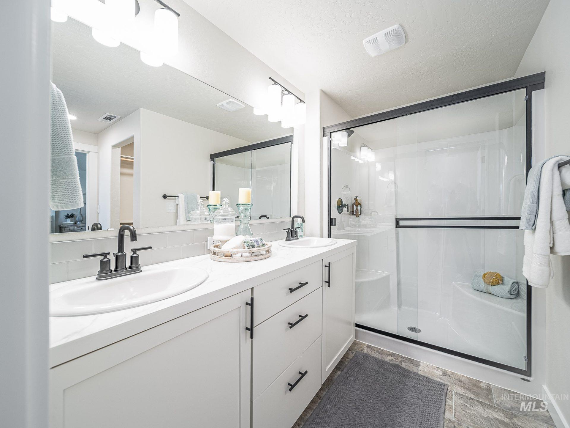 Full bathroom featuring double vanity, a stall shower, stone finish floors, and a spacious closet
