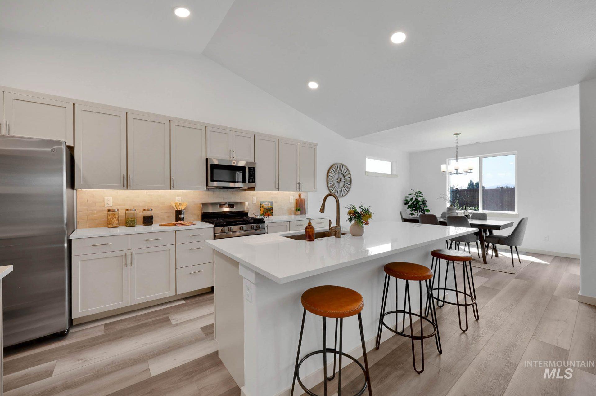 Kitchen with backsplash, stainless steel appliances, vaulted ceiling, a kitchen breakfast bar, and an island with sink
