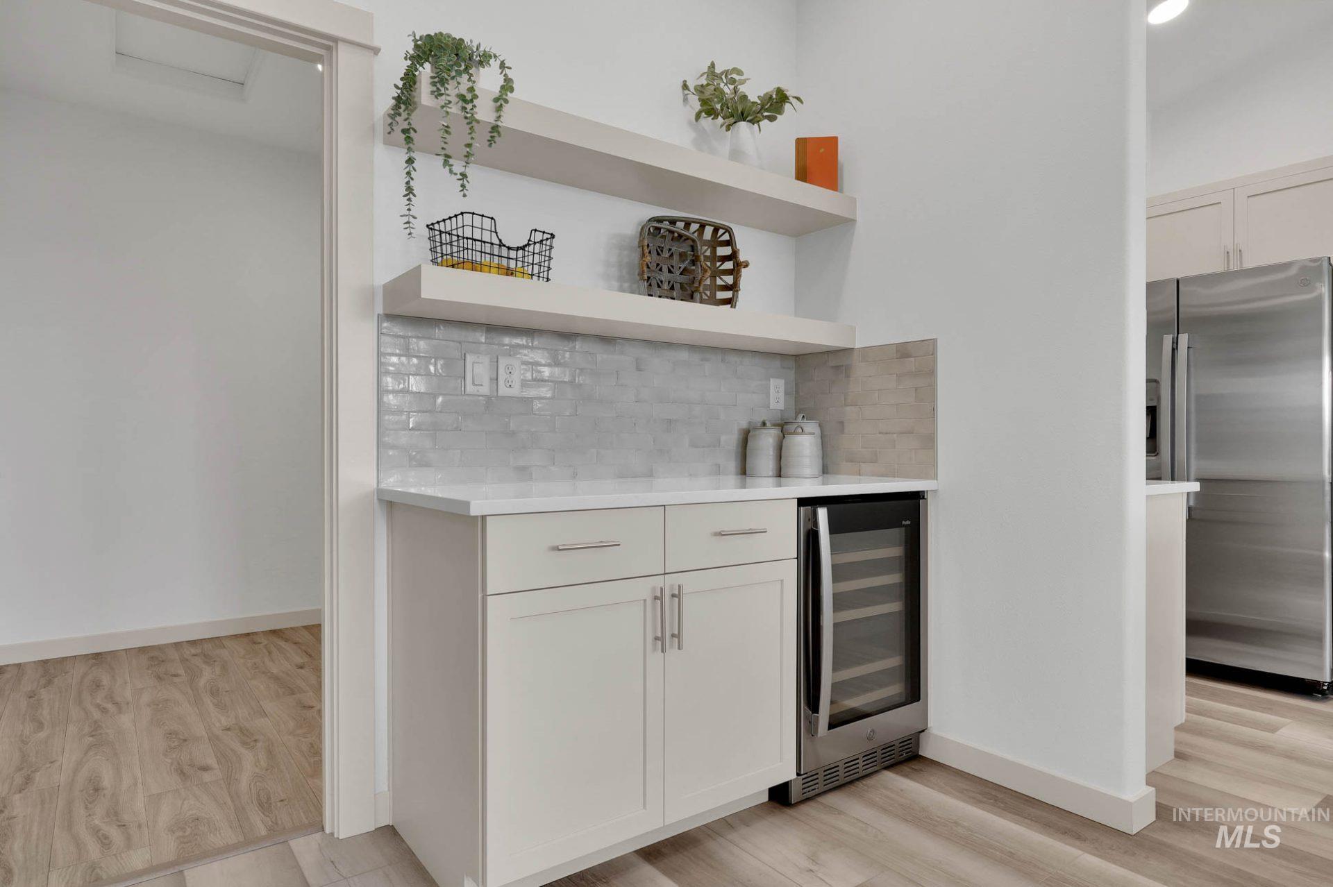 Indoor dry bar with stainless steel fridge, light stone countertops, decorative backsplash, open shelves, and wine cooler
