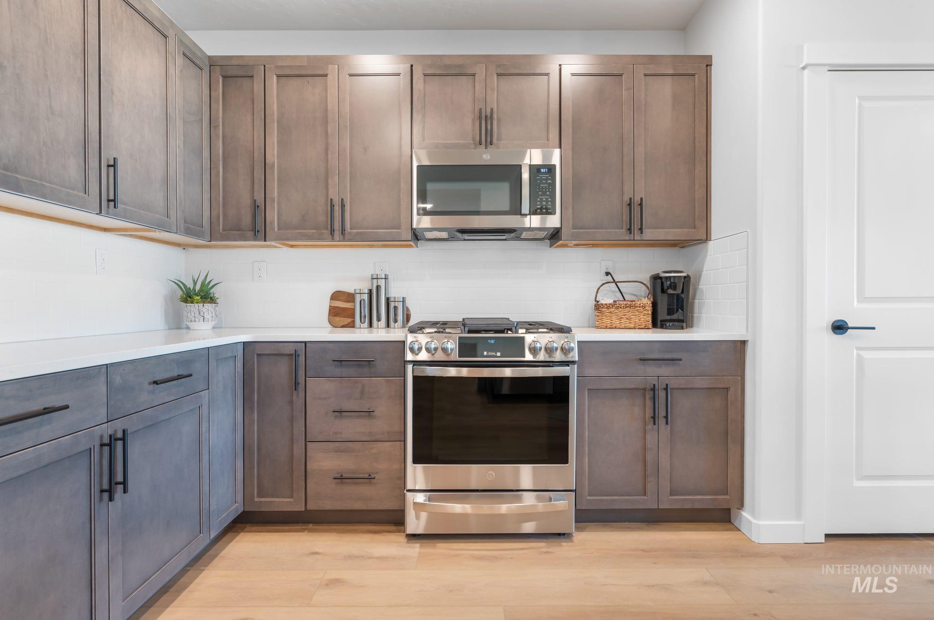Kitchen featuring appliances with stainless steel finishes, decorative backsplash, light stone countertops, and light wood-style flooring