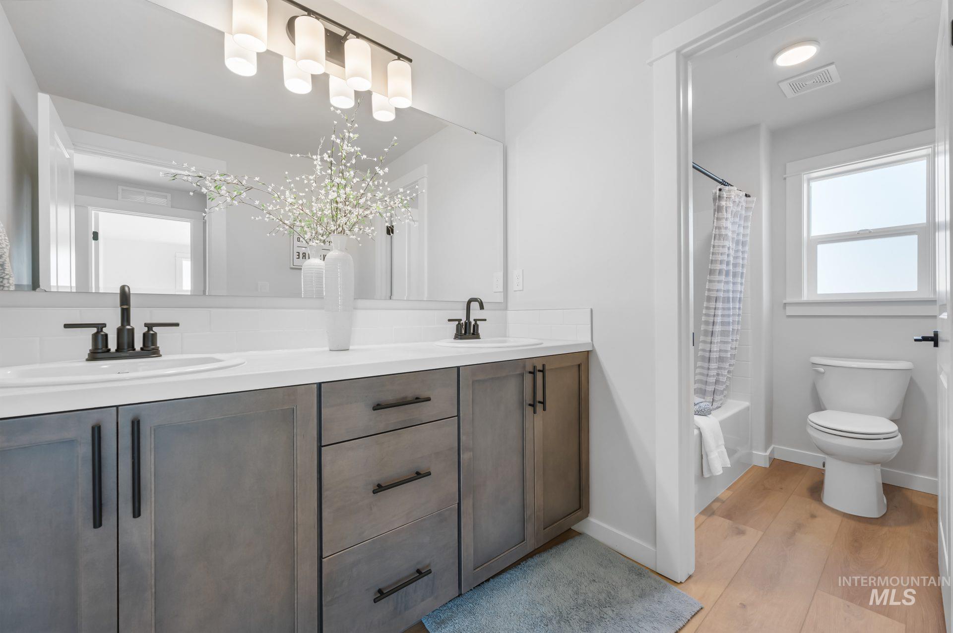 Bathroom featuring double vanity, shower / bath combo, and light wood-style floors