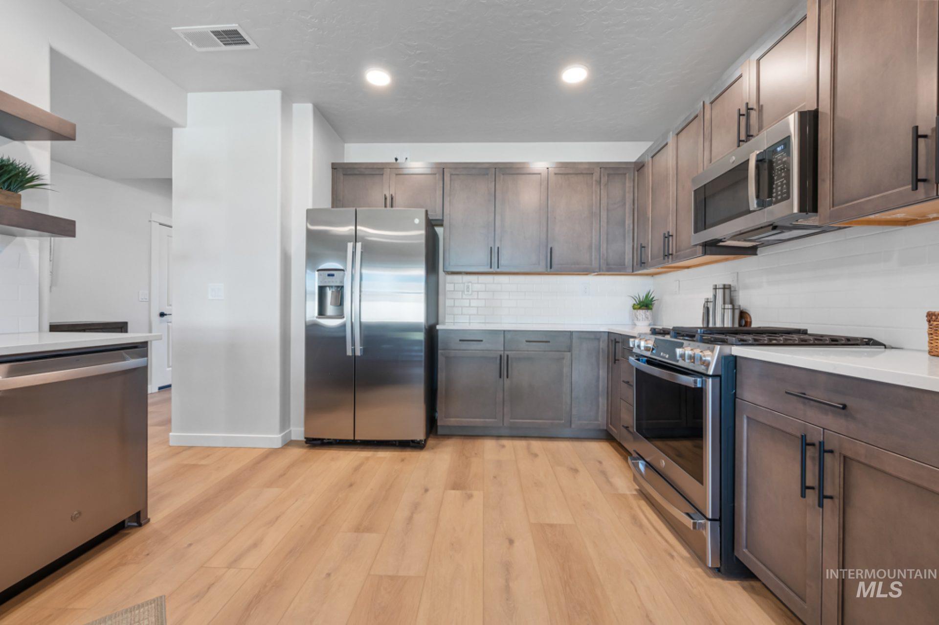 Kitchen featuring stainless steel appliances, tasteful backsplash, light wood finished floors, light stone counters, and dark brown cabinetry