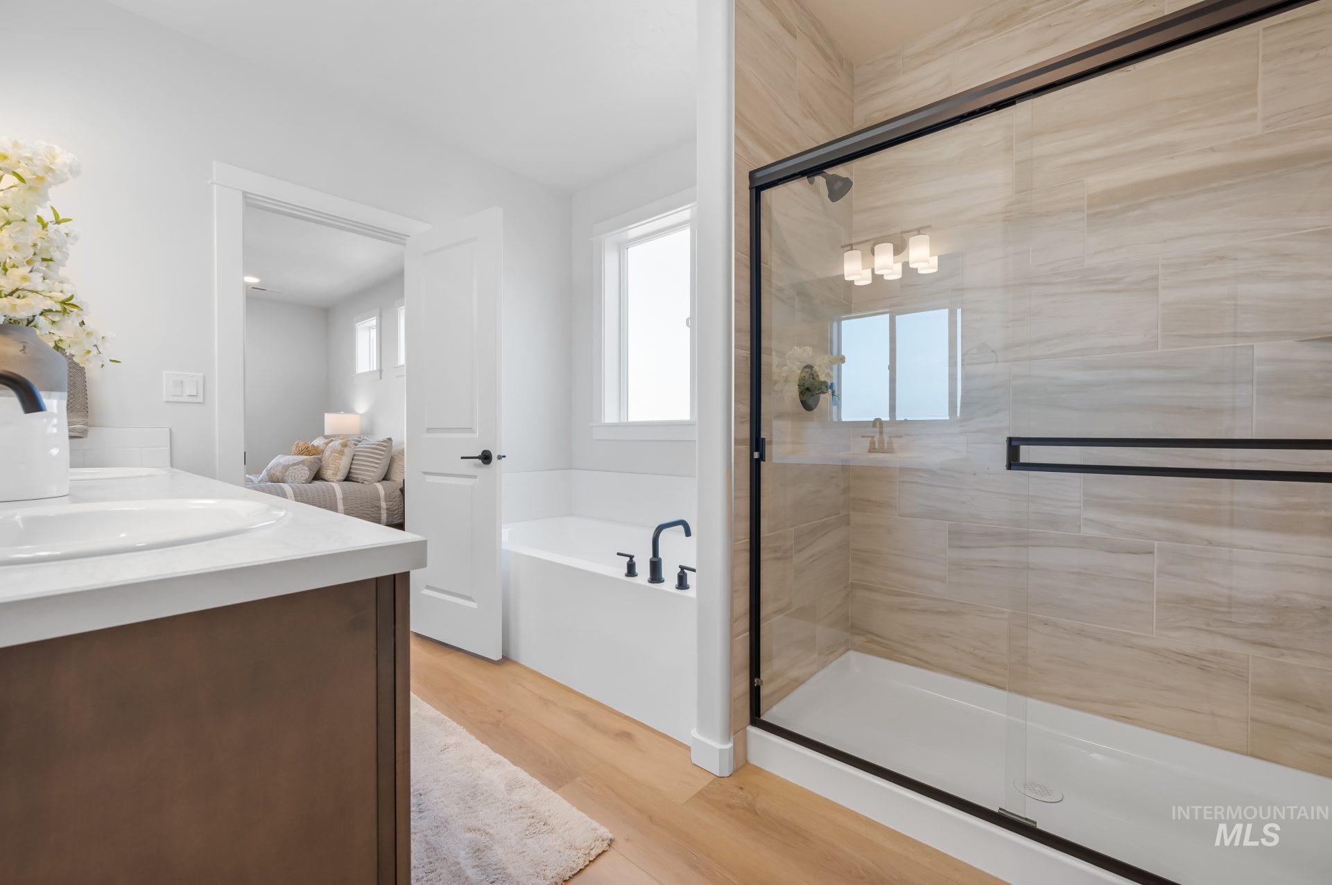 Bathroom with light wood-style floors, a garden tub, double vanity, and a stall shower