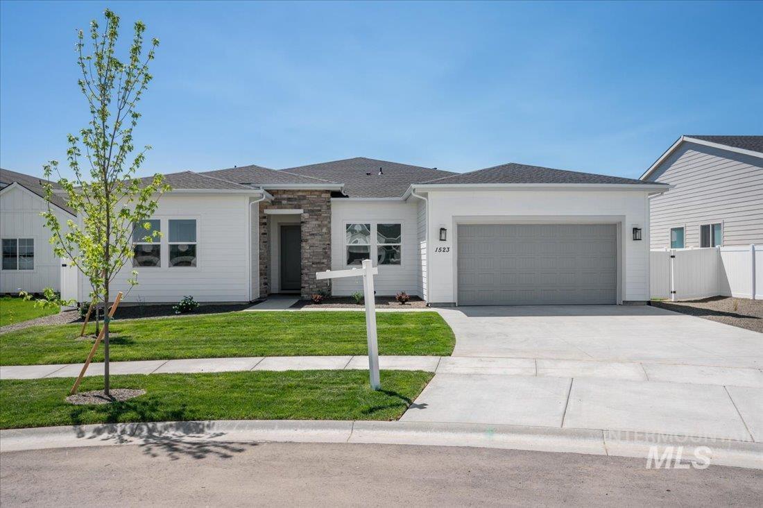 View of front of property featuring driveway, a garage, stone siding, and roof with shingles