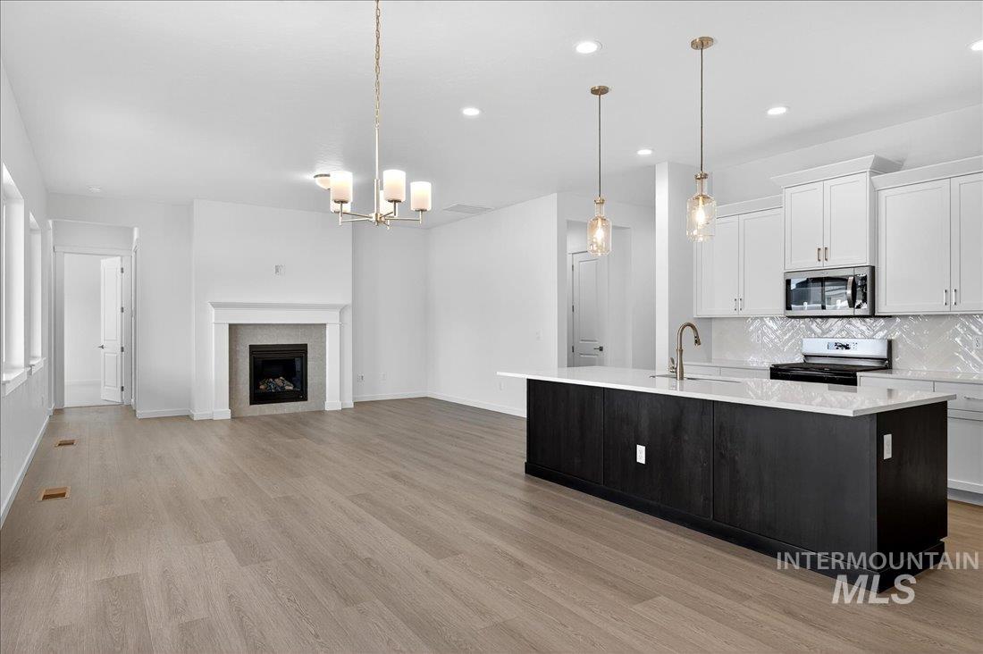 Kitchen featuring white cabinetry, an island with sink, decorative backsplash, hanging light fixtures, and range with electric stovetop