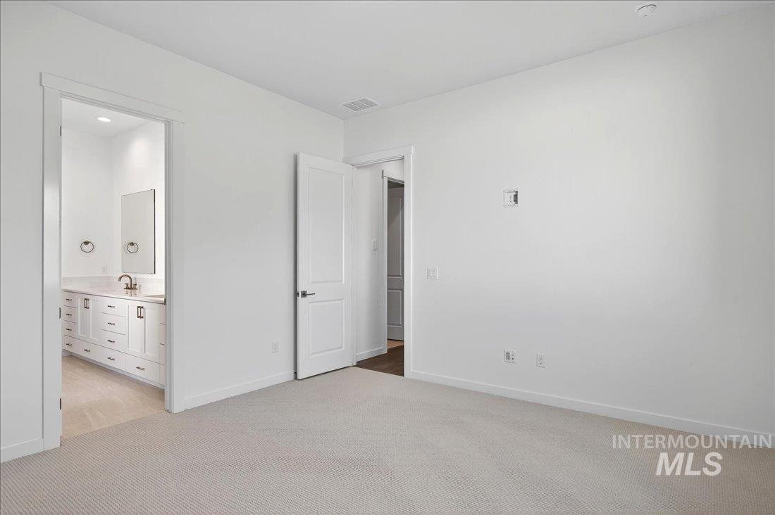 Unfurnished bedroom with light colored carpet, ensuite bath, and recessed lighting