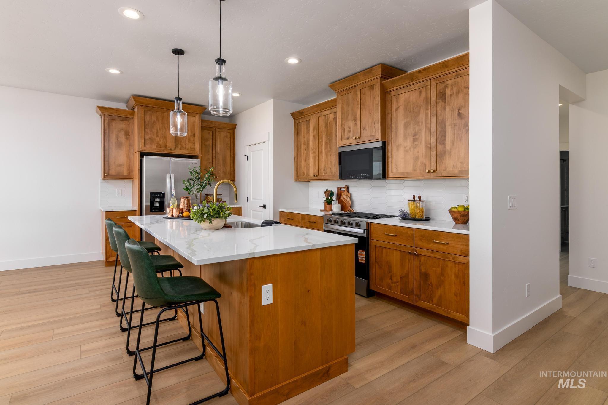 Kitchen with brown cabinets, a kitchen island with sink, appliances with stainless steel finishes, a kitchen bar, and recessed lighting