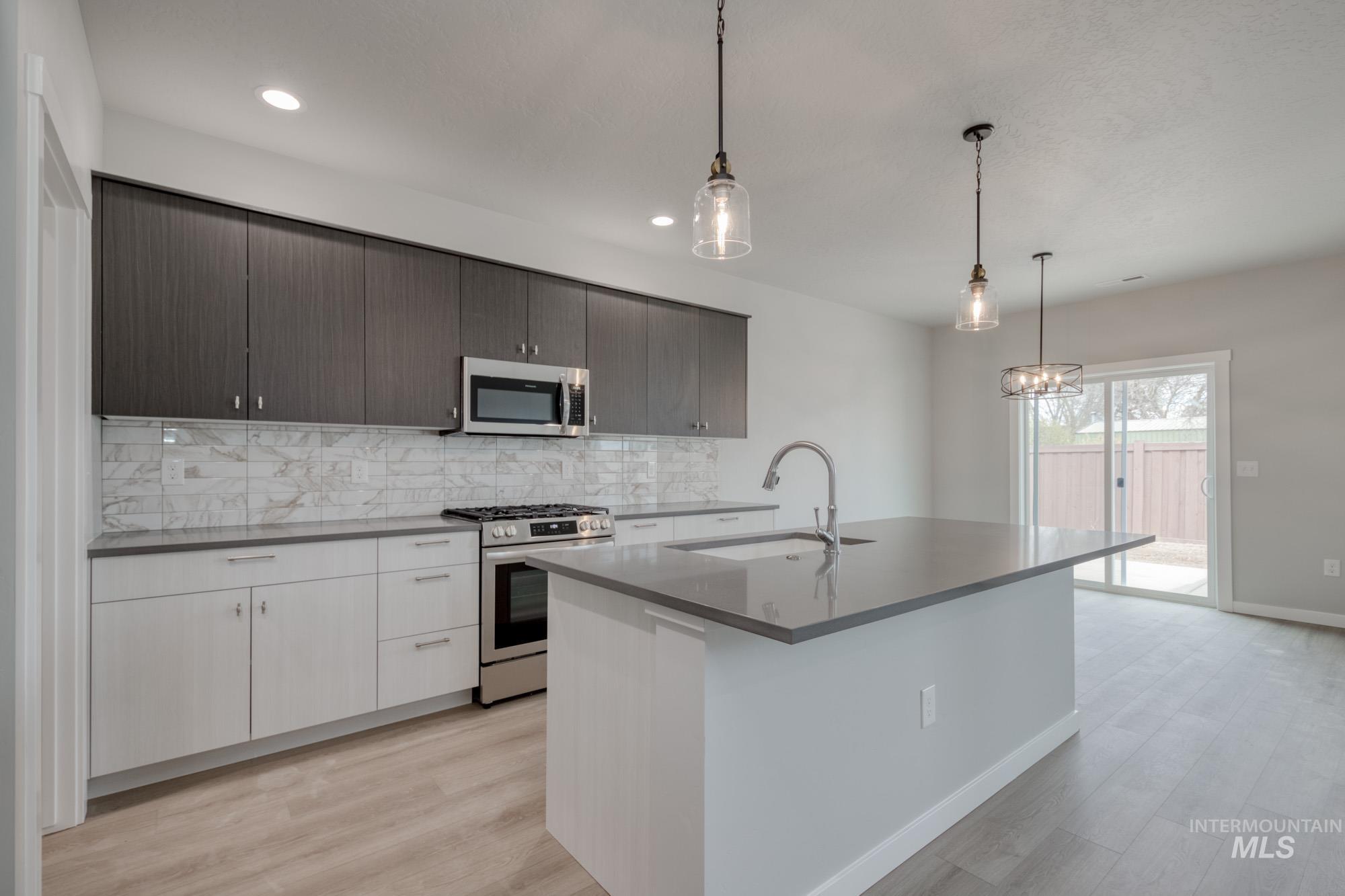 Kitchen with appliances with stainless steel finishes, pendant lighting, tasteful backsplash, light wood-style floors, and recessed lighting