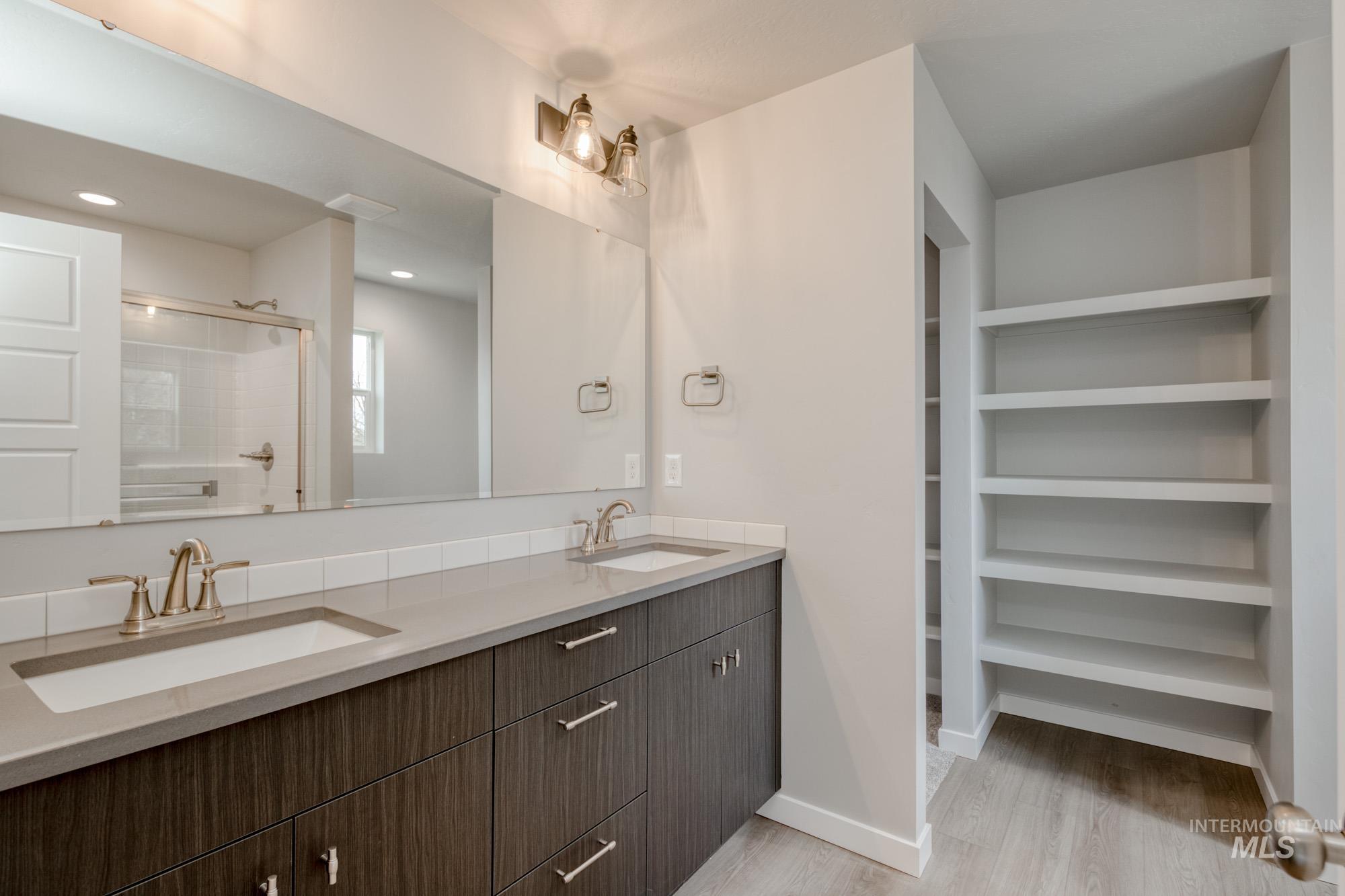 Full bath with double vanity, light wood-style floors, and a stall shower