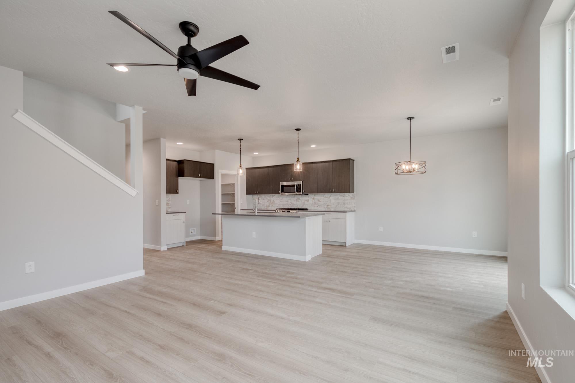 Unfurnished living room featuring a ceiling fan, light wood-type flooring, a chandelier, and recessed lighting