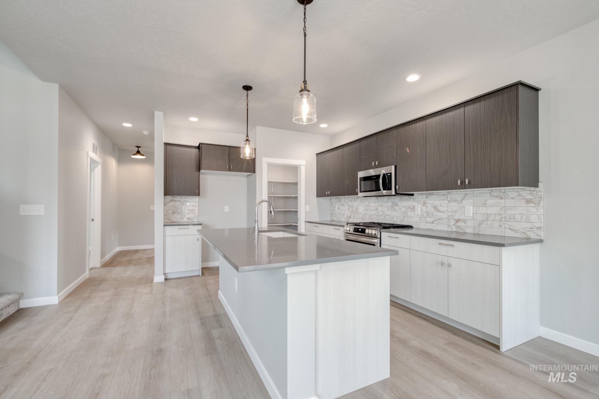 Kitchen featuring tasteful backsplash, modern cabinets, stainless steel appliances, light wood finished floors, and a kitchen island with sink