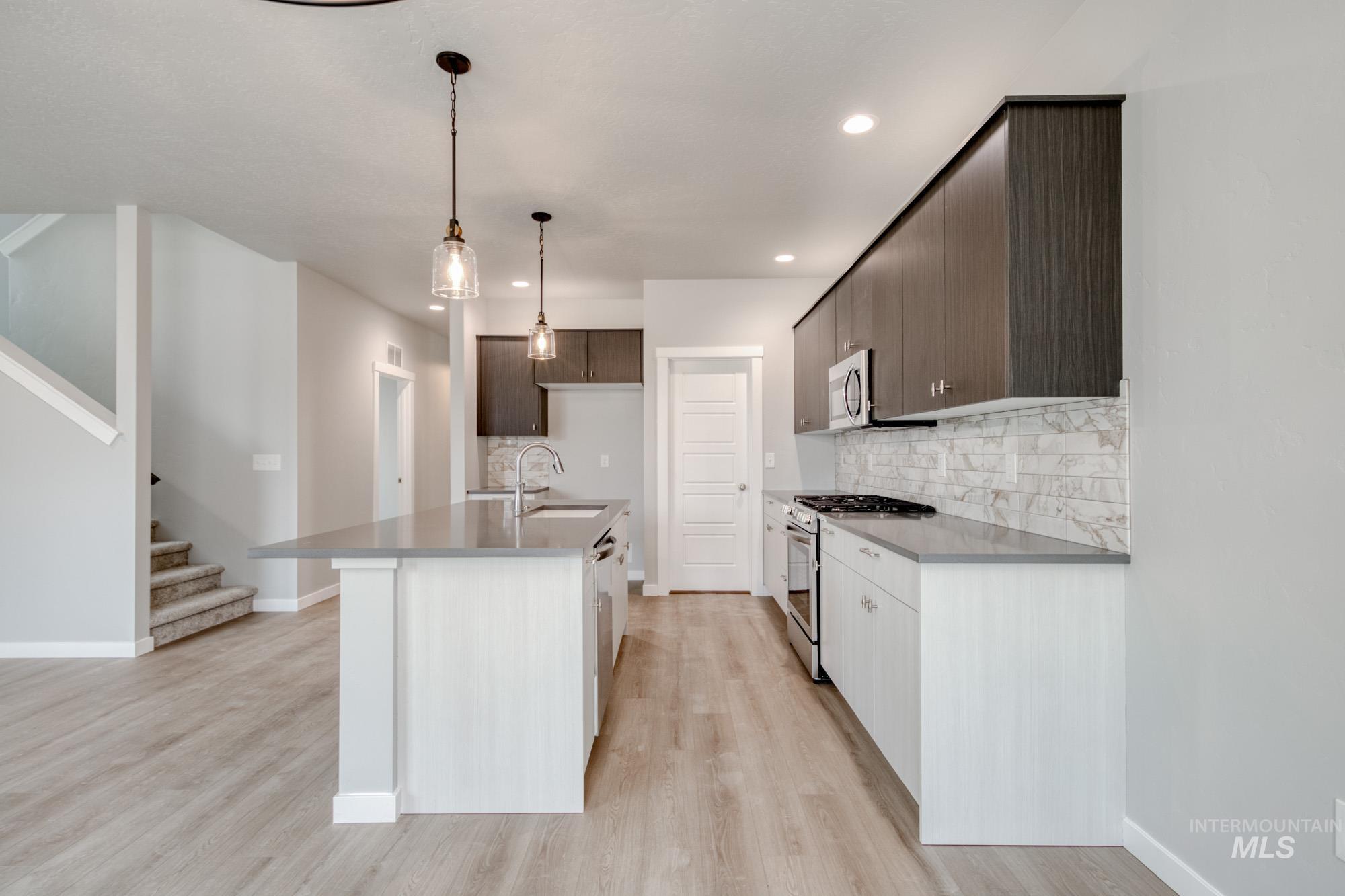 Kitchen with appliances with stainless steel finishes, a center island with sink, backsplash, hanging light fixtures, and light wood-style floors