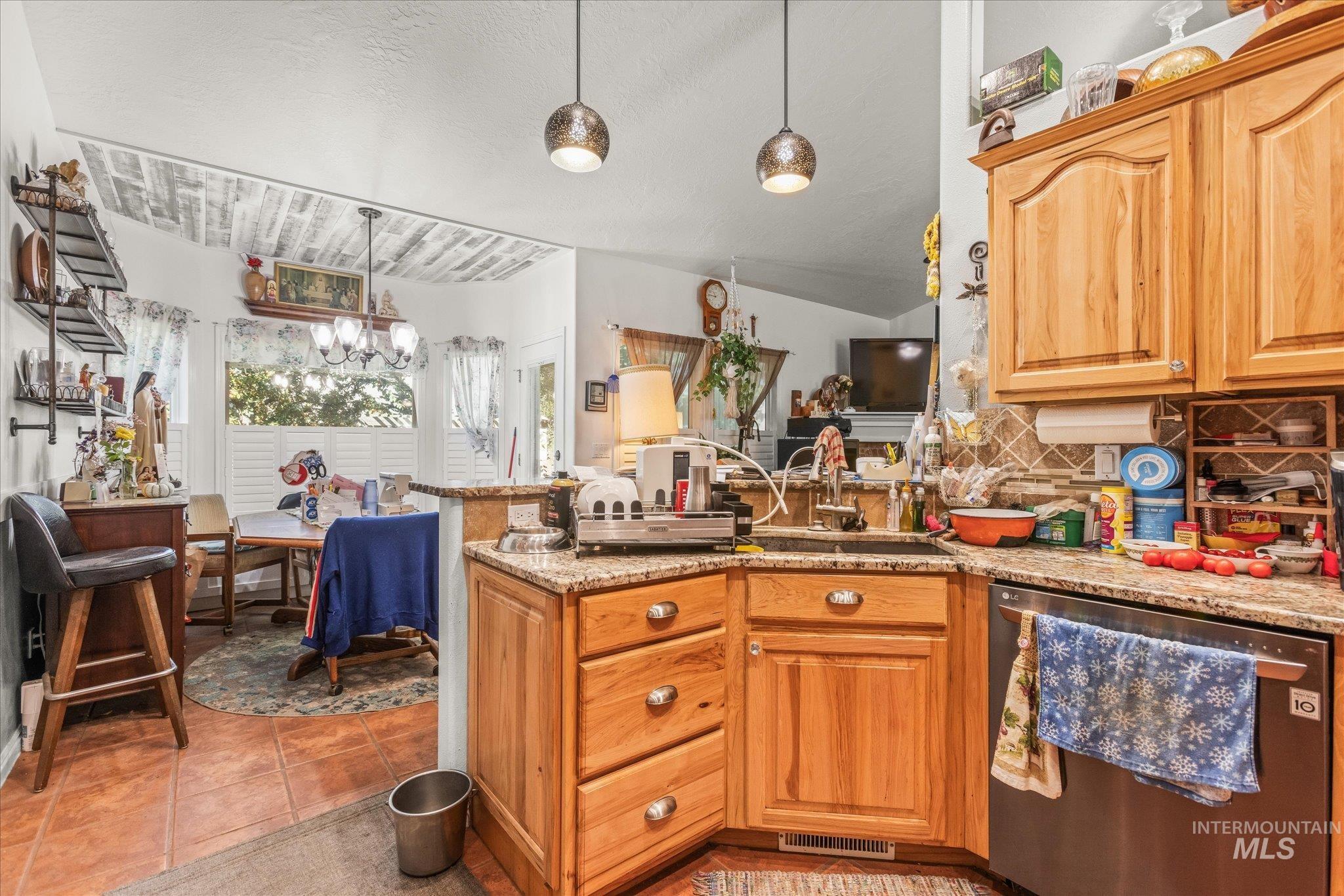 Kitchen featuring a peninsula, stainless steel dishwasher, tasteful backsplash, decorative light fixtures, and a textured ceiling