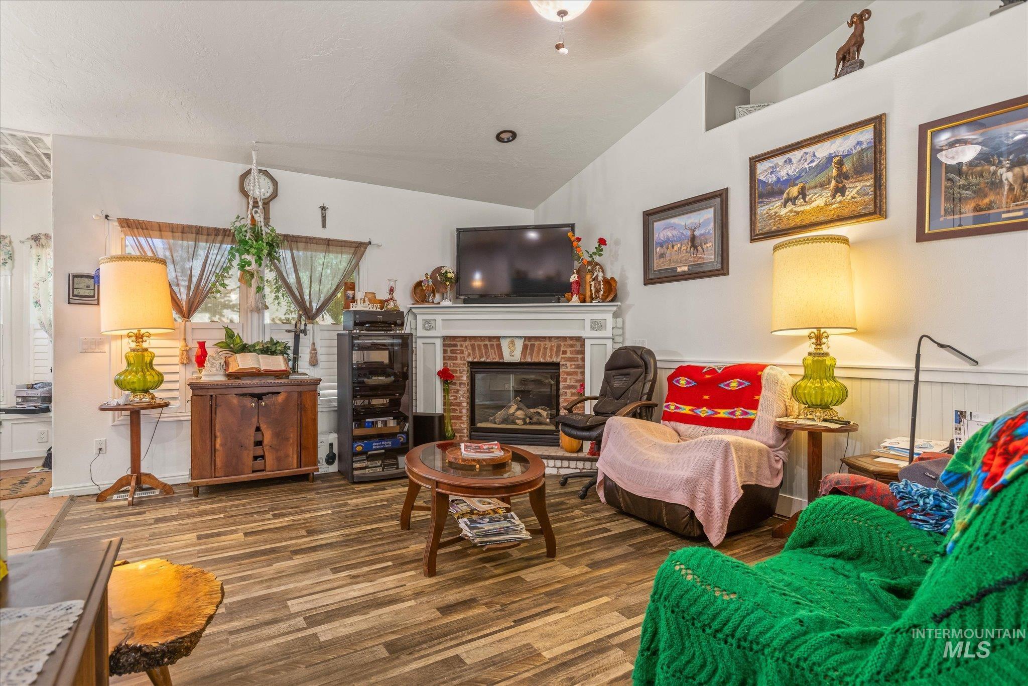 Living area with lofted ceiling, a brick fireplace, and wood finished floors