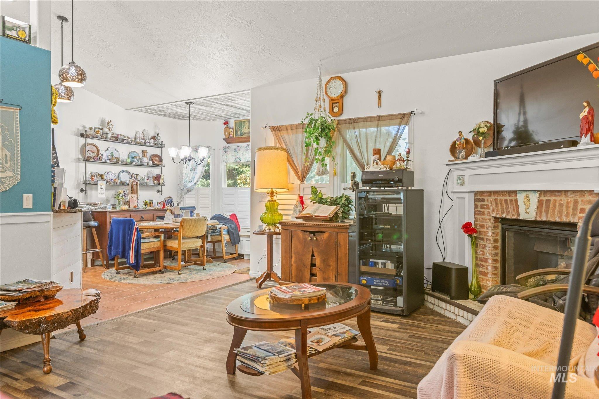 Living room featuring a brick fireplace, wood finished floors, a textured ceiling, and a chandelier