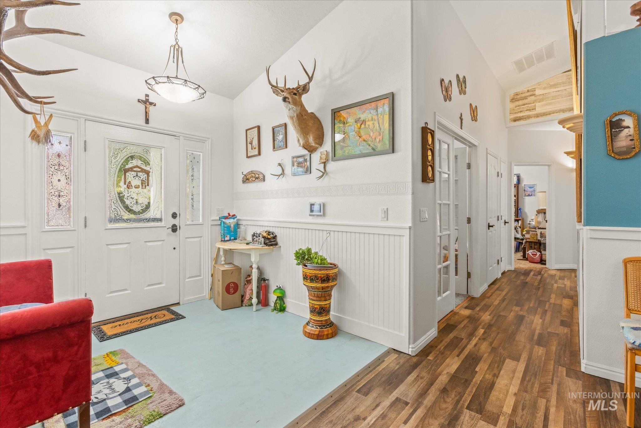 Foyer entrance with dark wood-style floors, lofted ceiling, and wainscoting