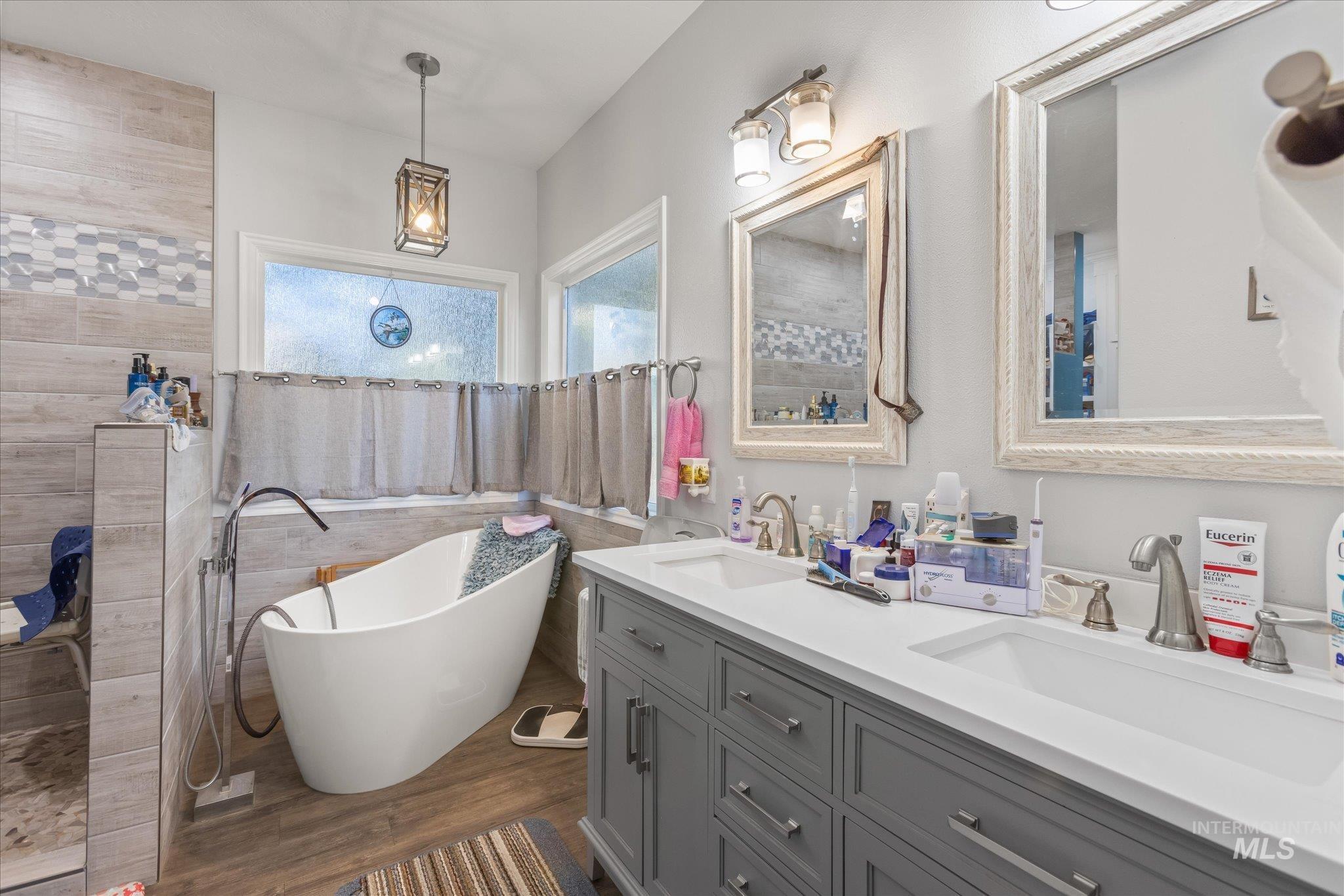 Bathroom featuring a freestanding tub, double vanity, dark wood-style floors, walk in shower, and tile walls