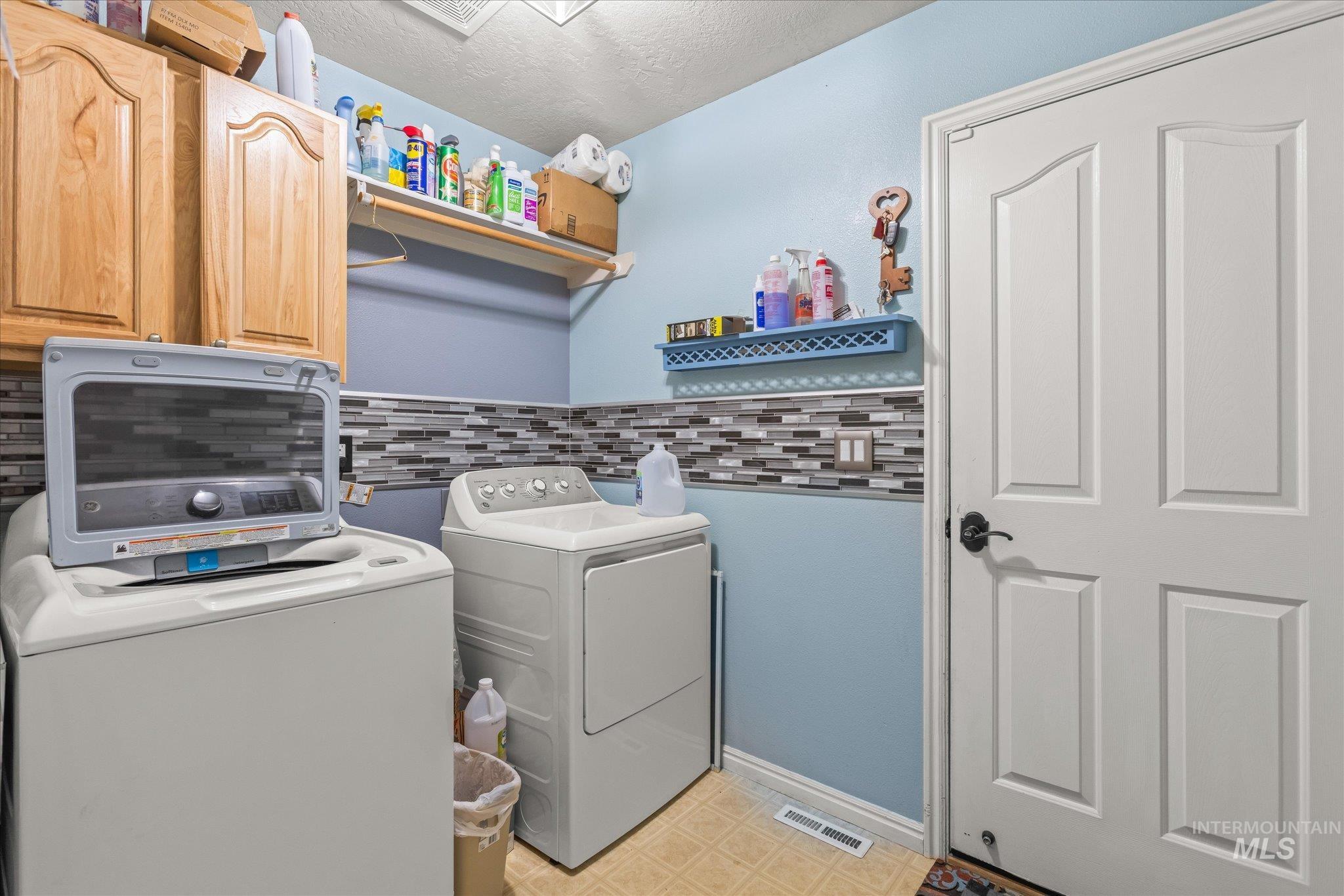 Washroom featuring a textured ceiling, separate washer and dryer, cabinet space, and light floors