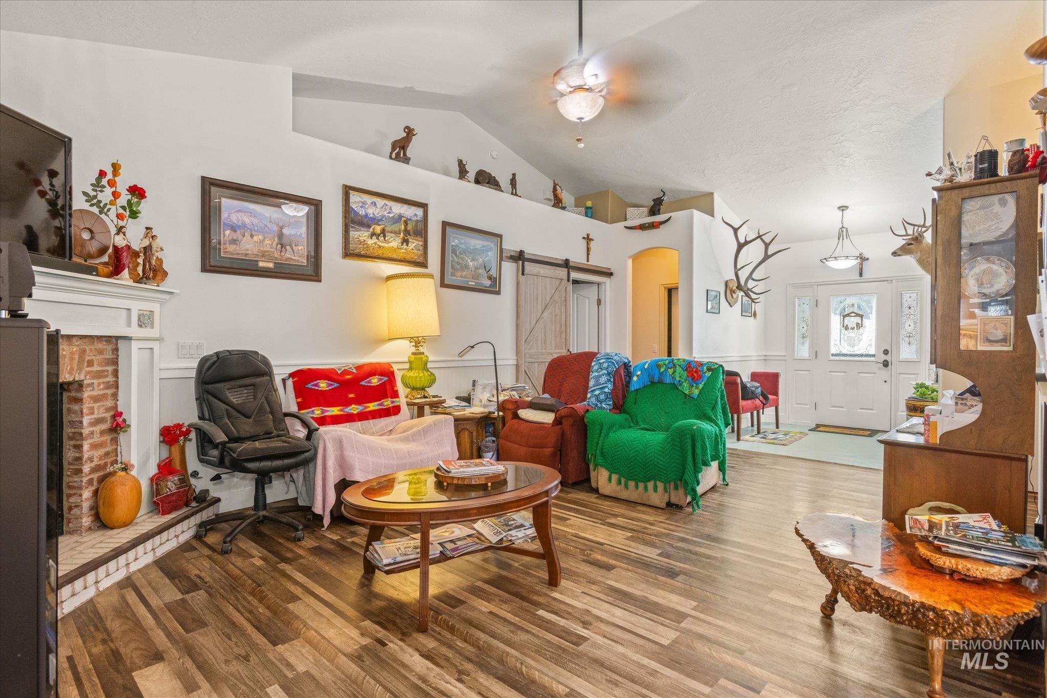 Living area with arched walkways, a barn door, wood finished floors, a brick fireplace, and lofted ceiling
