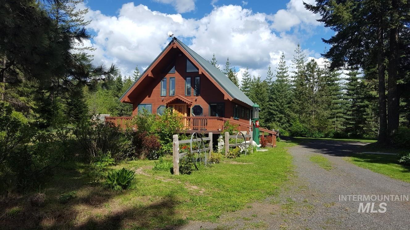View of front of house featuring gravel driveway, a view of trees, a metal roof, and a deck