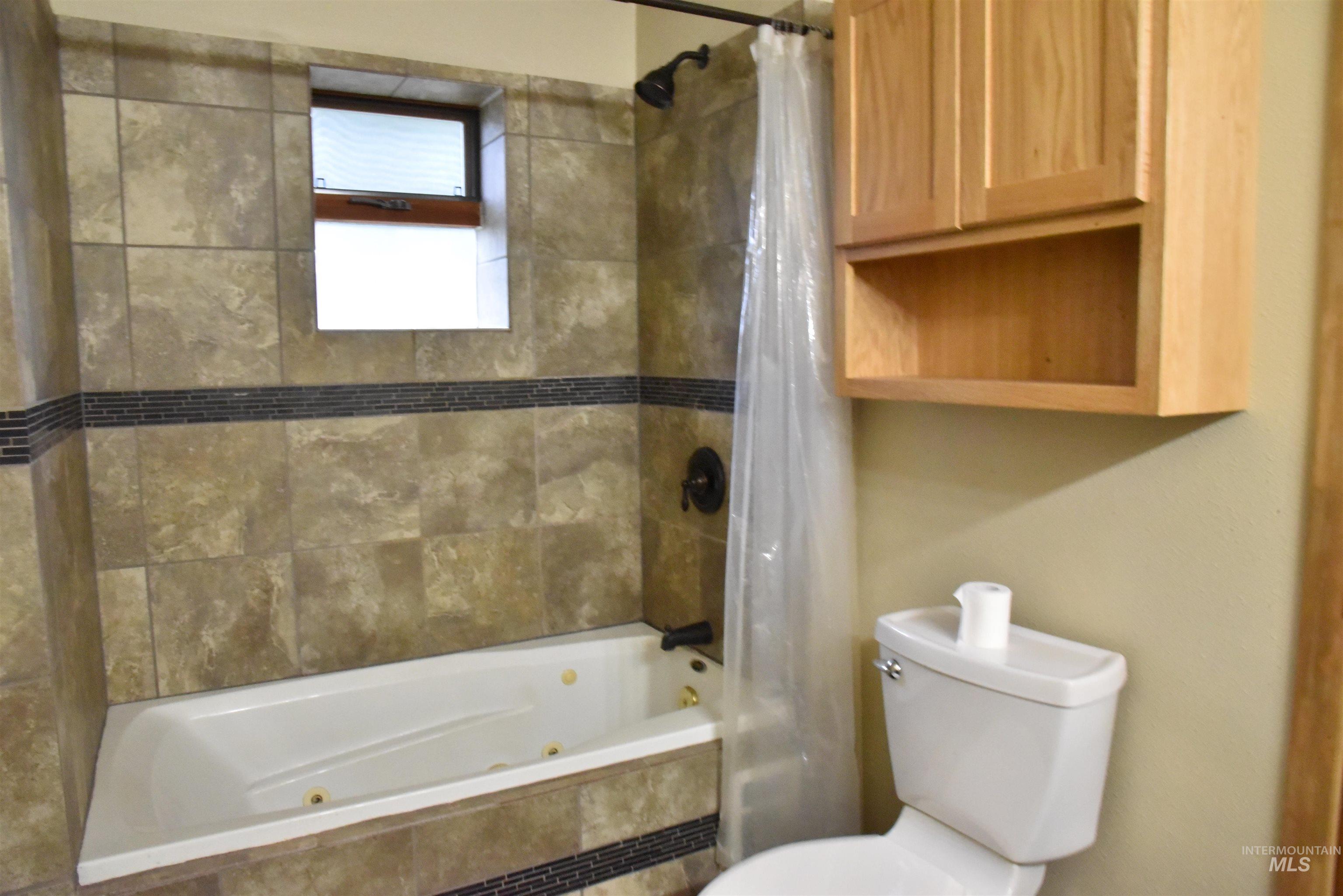 Bathroom featuring a combined bath / shower with jetted tub and toilet