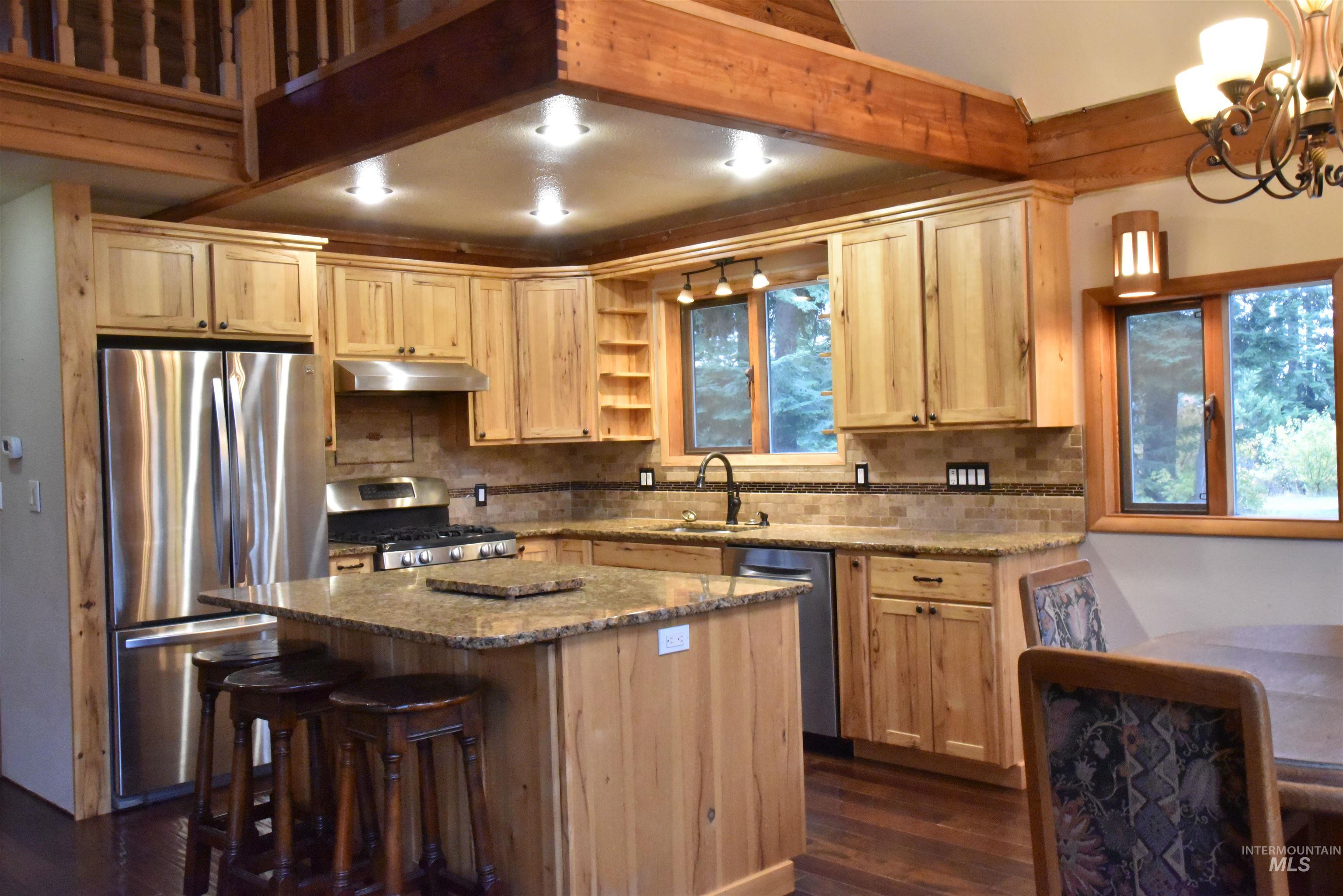 Kitchen with dark stone counters, appliances with stainless steel finishes, dark wood-type flooring, tasteful backsplash, and a center island