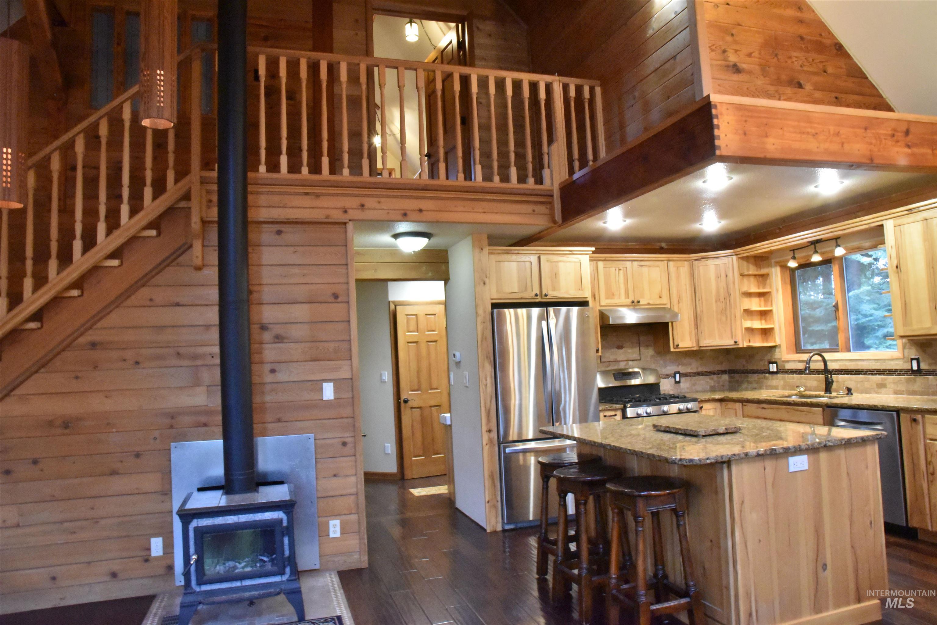 Kitchen with wooden walls, dark stone countertops, appliances with stainless steel finishes, a wood stove, and a kitchen island