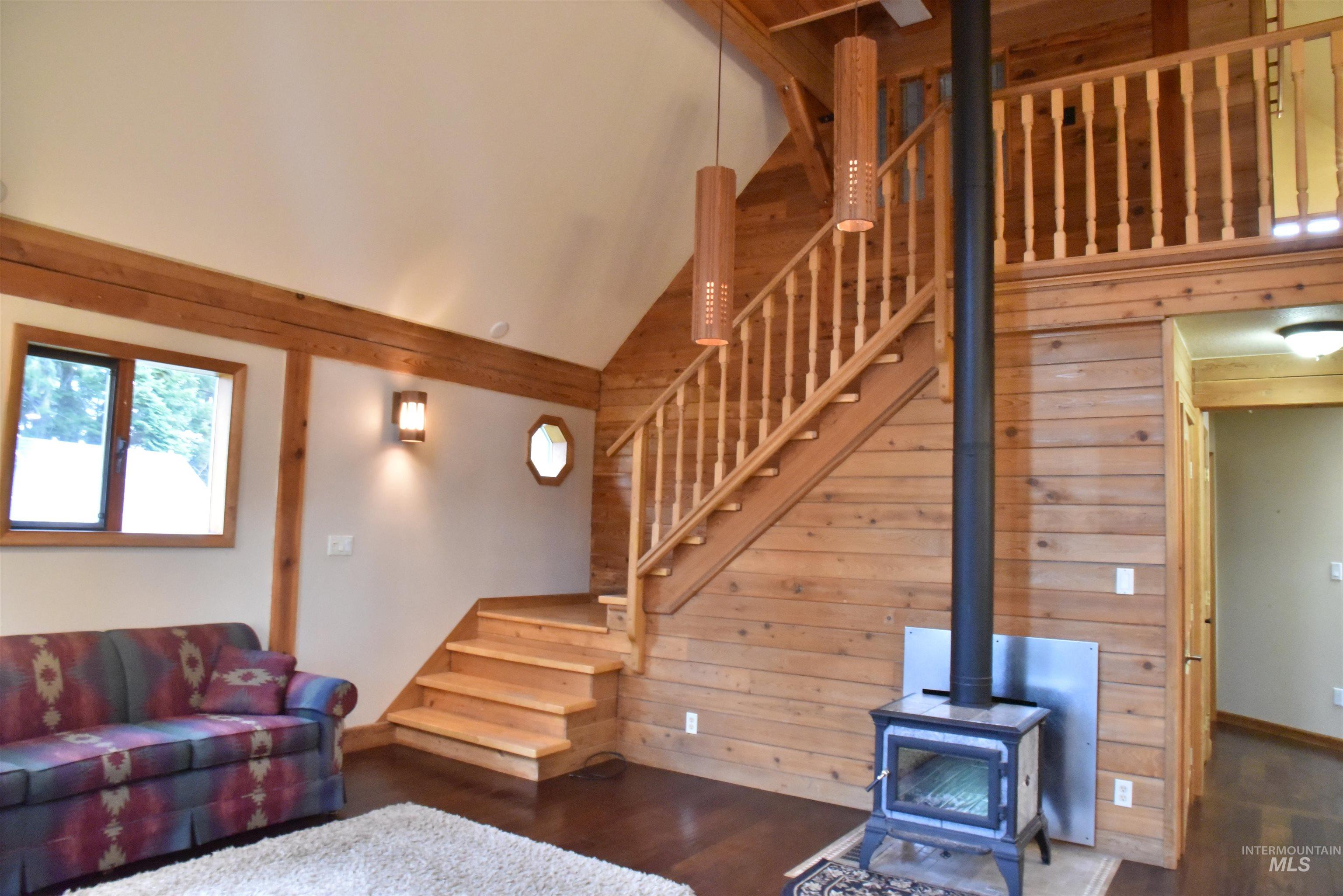 Living area featuring a wood stove, wood finished floors, stairway, wood walls, and high vaulted ceiling