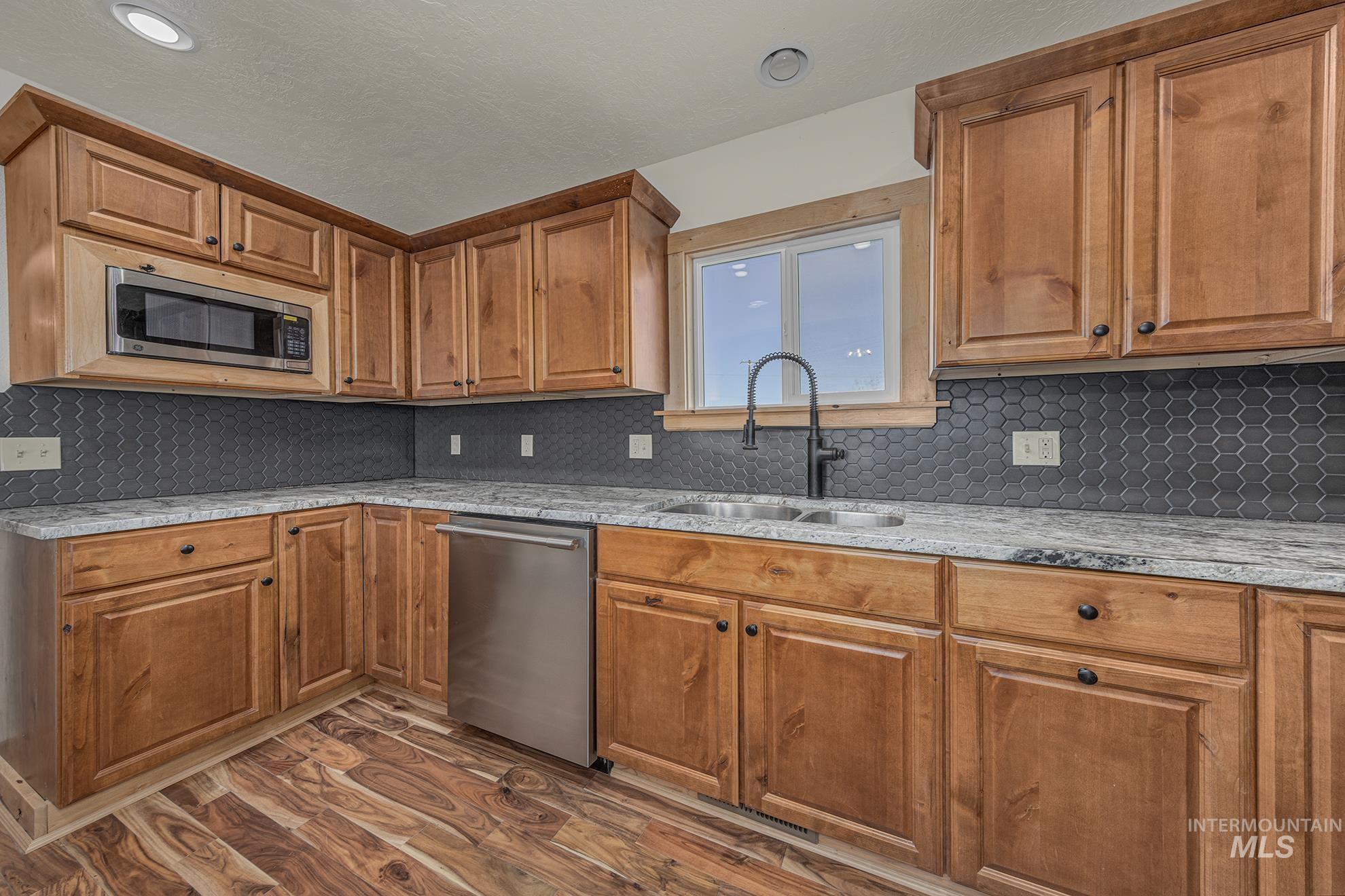 Kitchen with tasteful backsplash, brown cabinets, appliances with stainless steel finishes, and light stone countertops