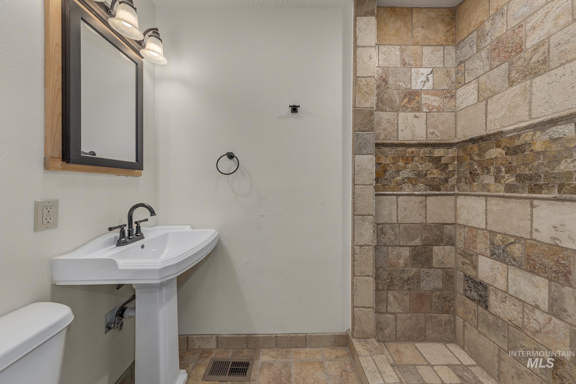 Full bath with stone tile floors and a tile shower
