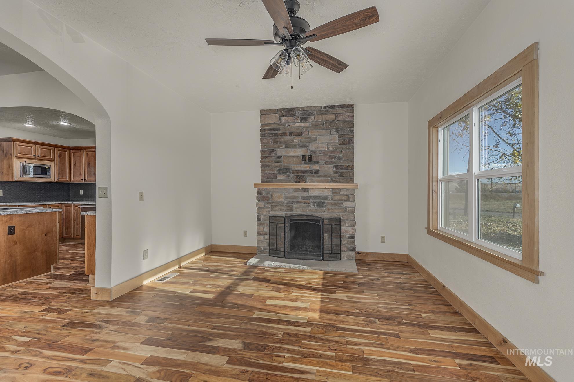 Unfurnished living room with arched walkways, light wood-type flooring, a fireplace, and ceiling fan