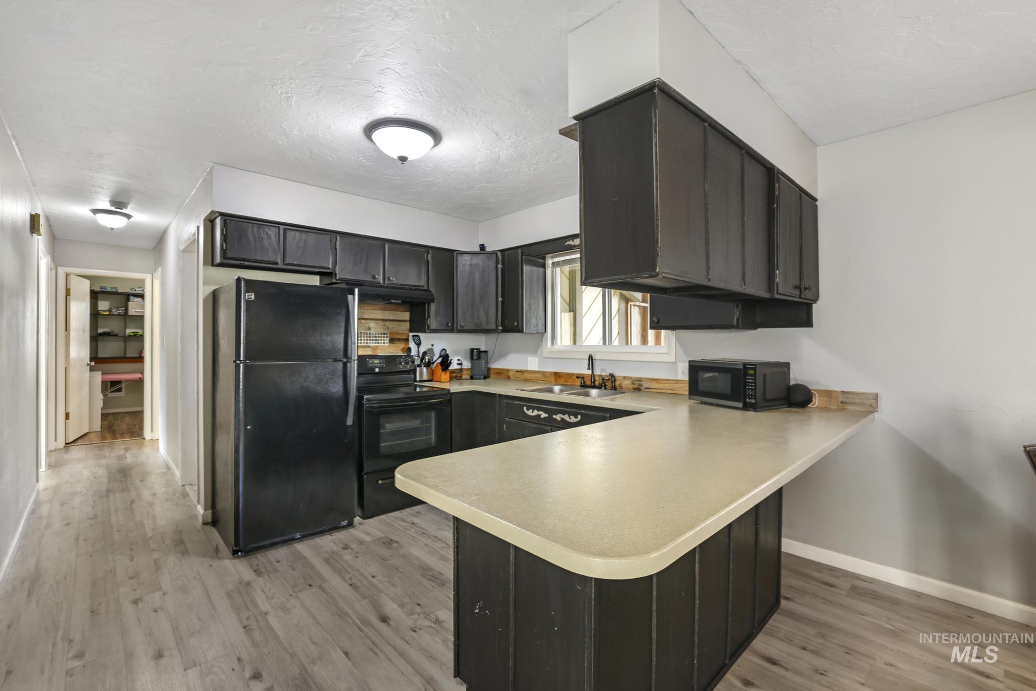 Kitchen featuring black appliances, a peninsula, dark cabinets, light countertops, and light wood-type flooring