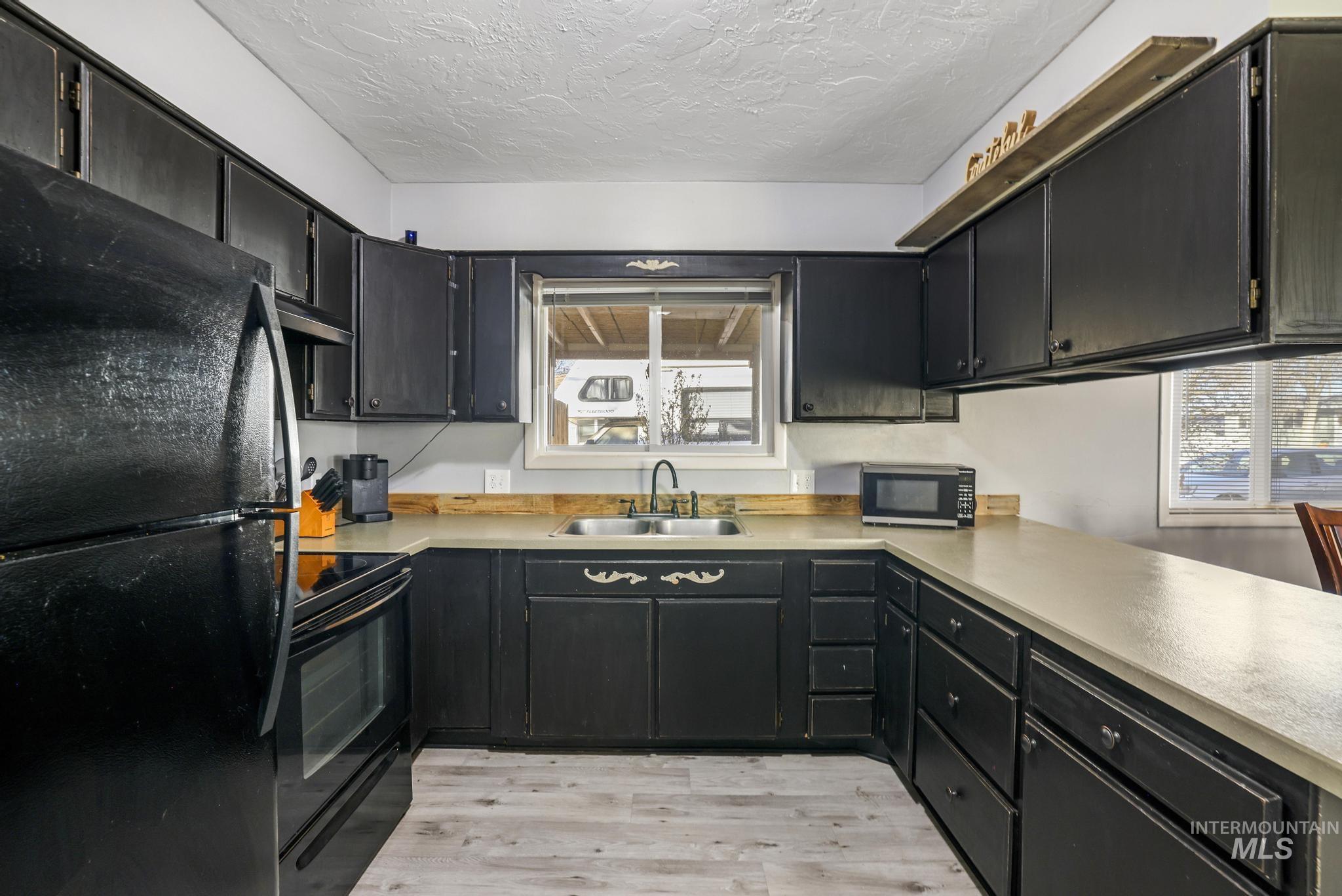 Kitchen with dark cabinets, black appliances, light wood finished floors, light countertops, and a textured ceiling