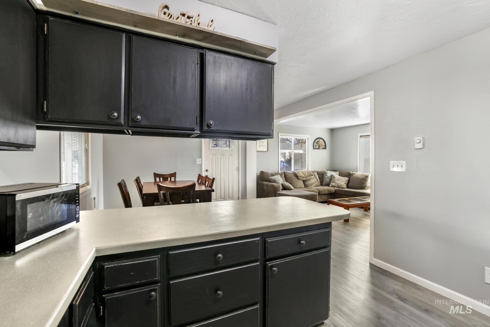 Kitchen featuring dark cabinets, stainless steel microwave, open floor plan, light countertops, and dark wood finished floors