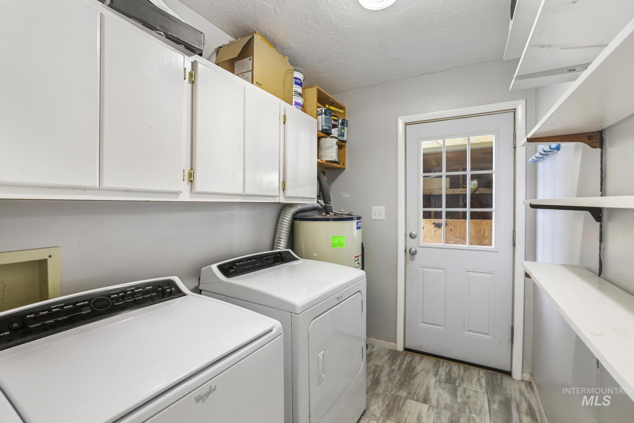 Washroom with electric water heater, washing machine and clothes dryer, cabinet space, light wood finished floors, and a textured ceiling