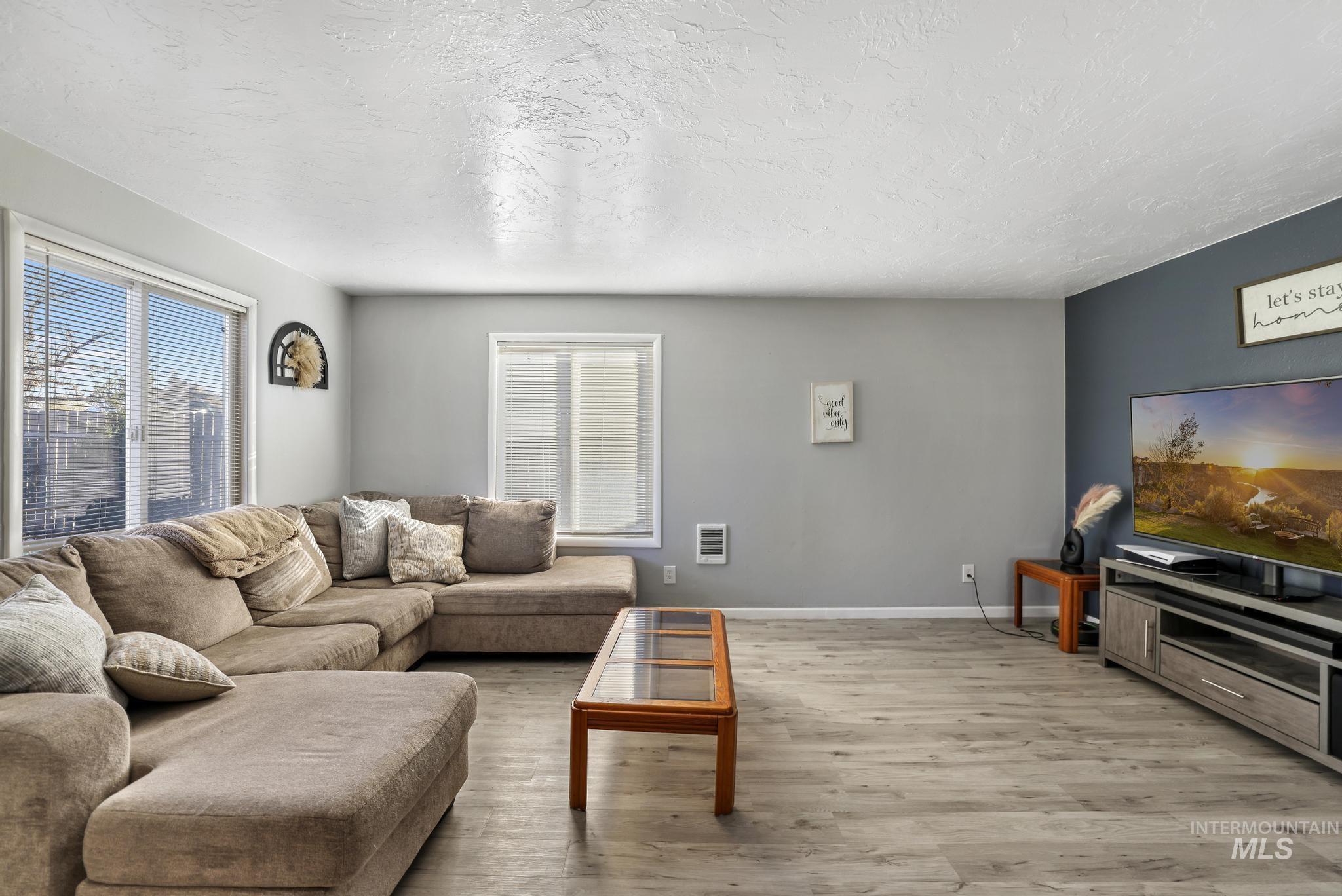 Living room featuring light wood-type flooring, healthy amount of natural light, a textured ceiling, and heating unit