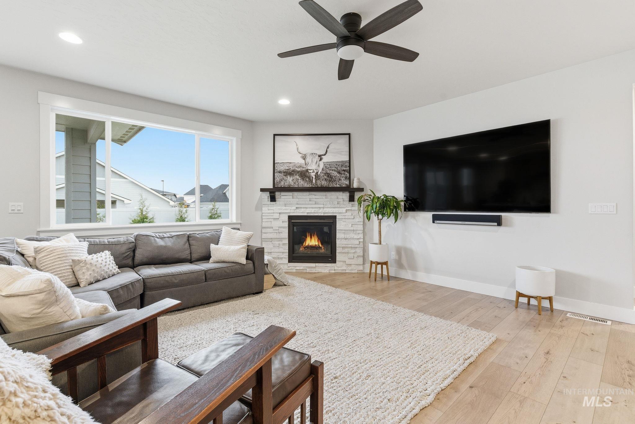 Living area with light wood finished floors, a stone fireplace, a ceiling fan, and recessed lighting