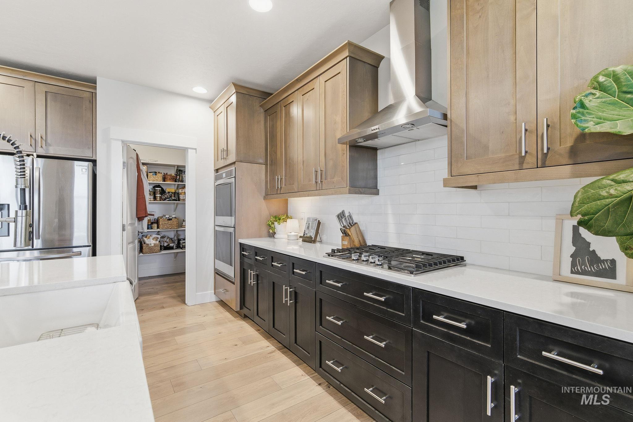 Kitchen featuring wall chimney range hood, light stone counters, appliances with stainless steel finishes, light wood-style flooring, and recessed lighting