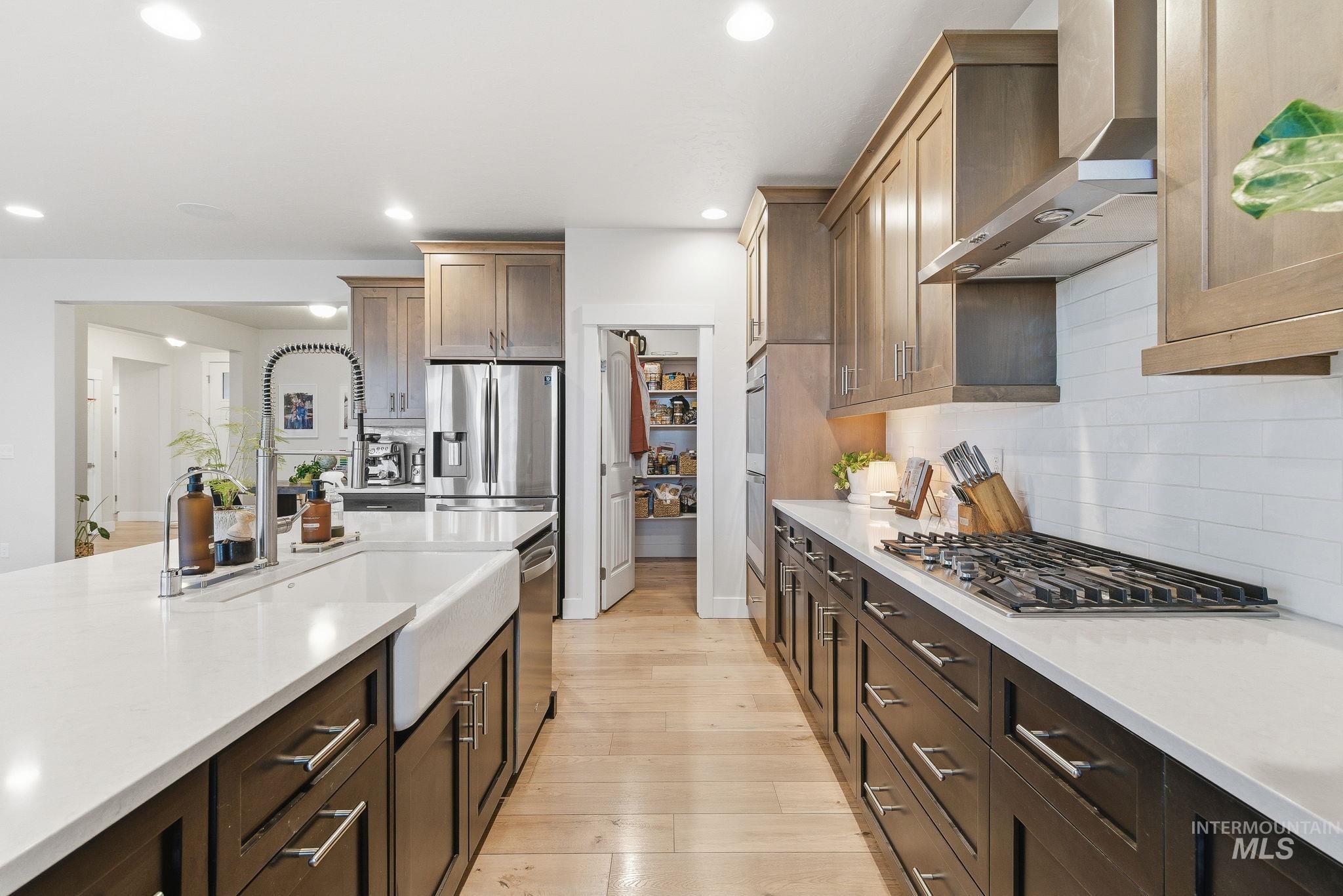Kitchen with wall chimney exhaust hood, light wood-style flooring, light stone counters, dark brown cabinets, and appliances with stainless steel finishes