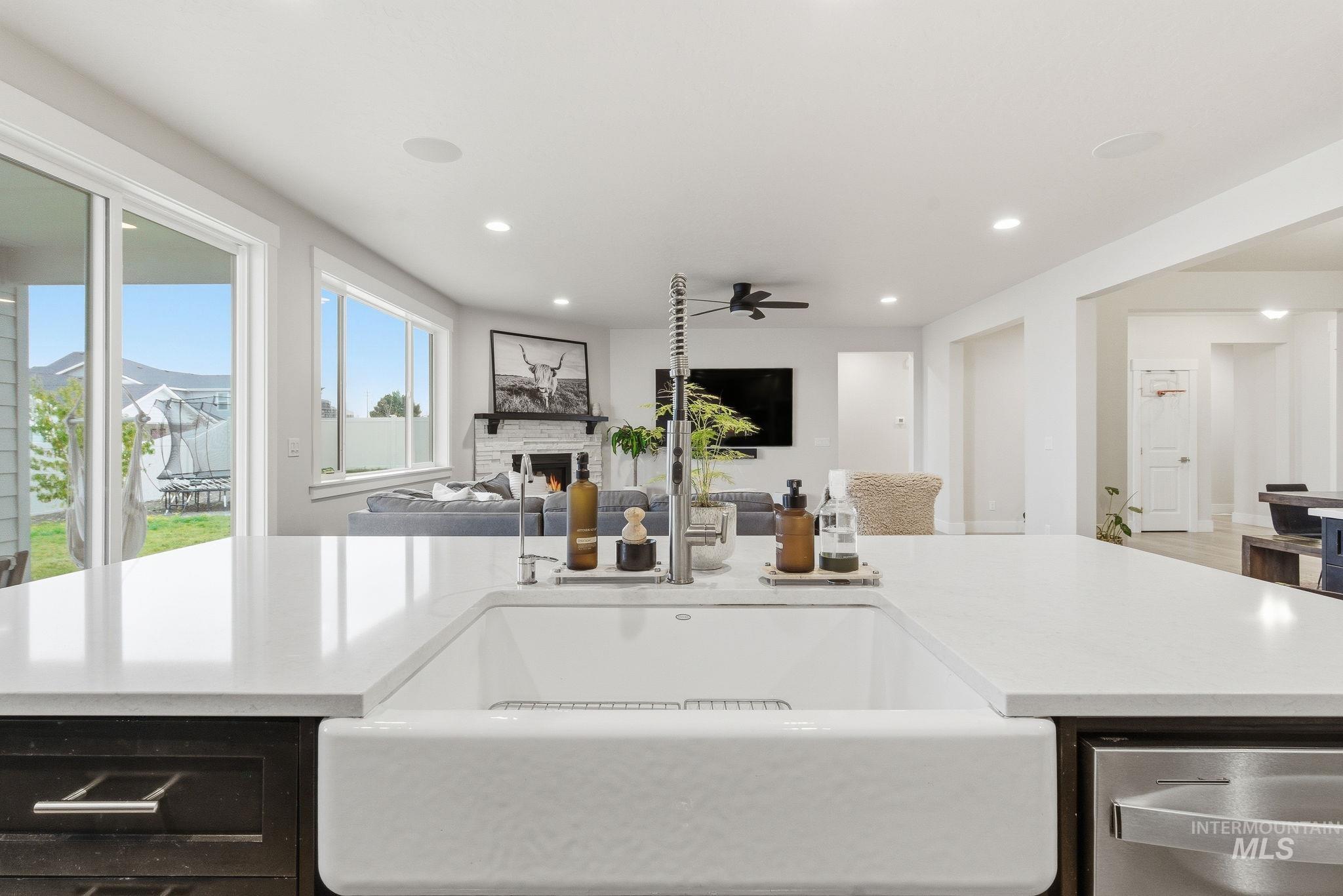 Kitchen featuring light stone counters, stainless steel dishwasher, a warm lit fireplace, recessed lighting, and open floor plan
