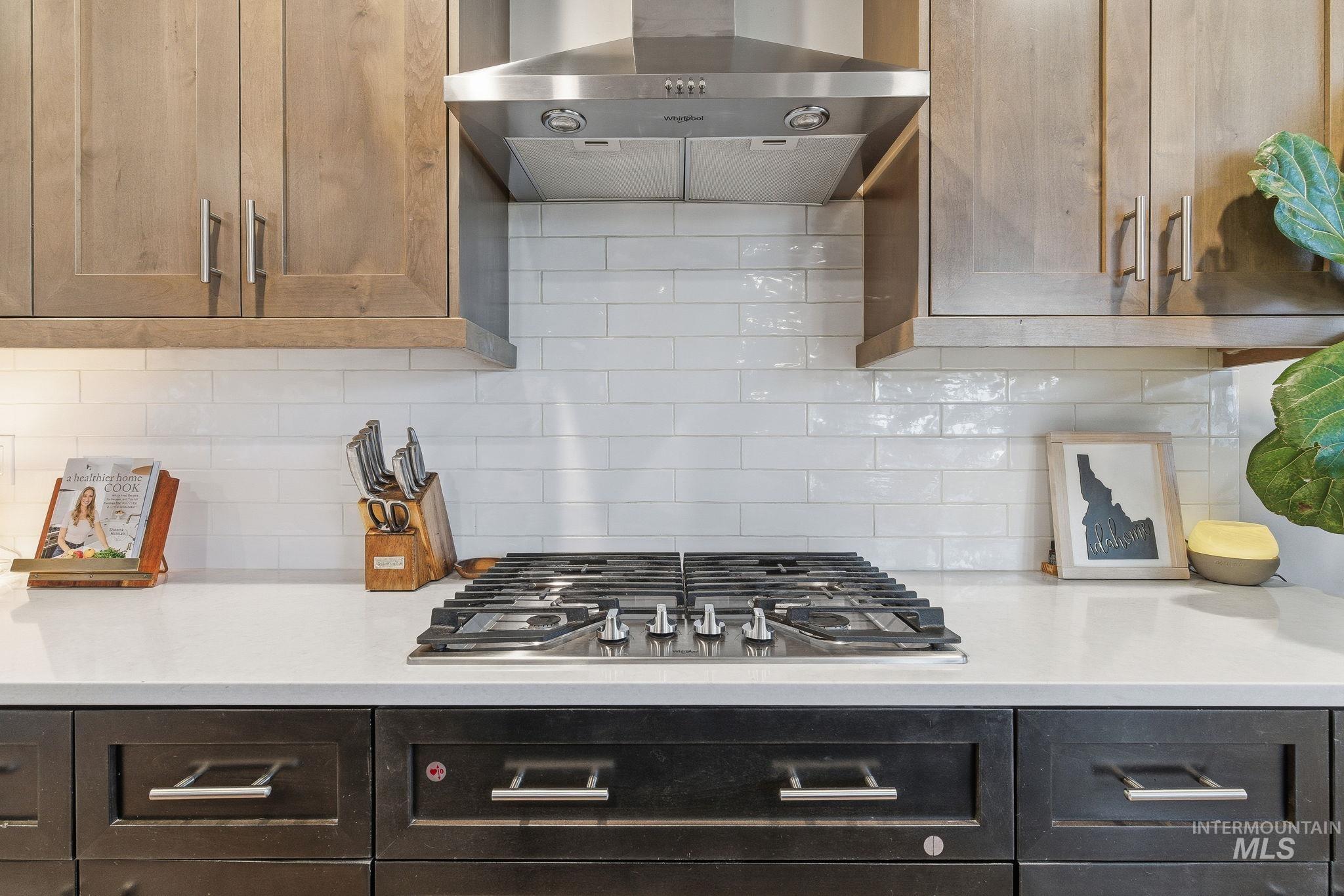 Kitchen with ventilation hood, decorative backsplash, stainless steel gas cooktop, and light stone counters