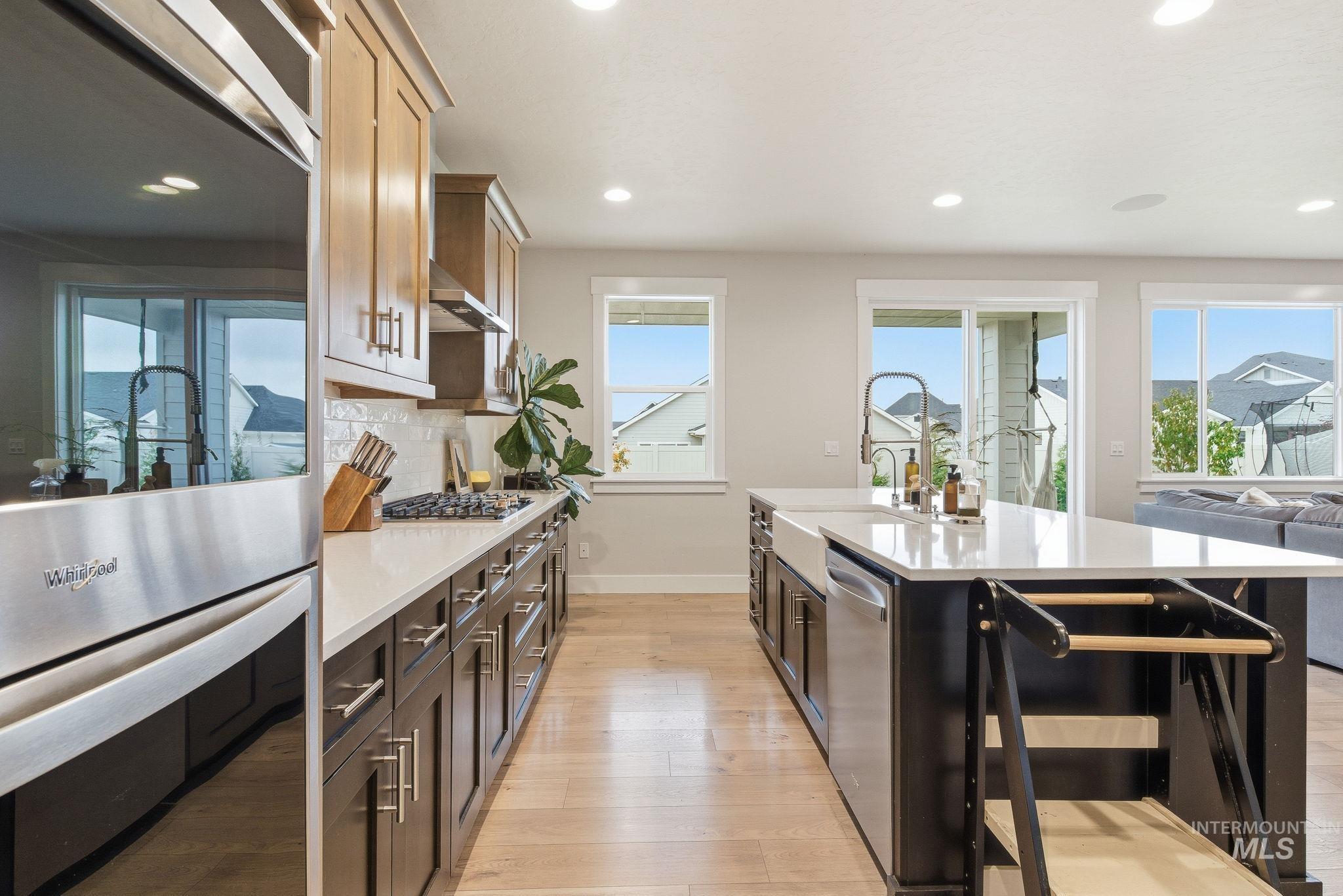 Kitchen with appliances with stainless steel finishes, recessed lighting, light wood-style flooring, light stone counters, and an island with sink