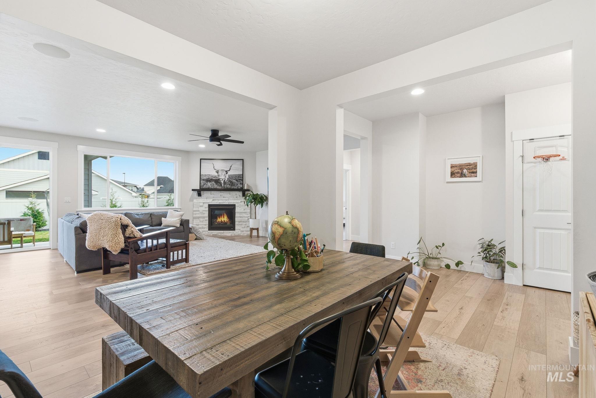 Dining space featuring light wood finished floors, a stone fireplace, a ceiling fan, and recessed lighting
