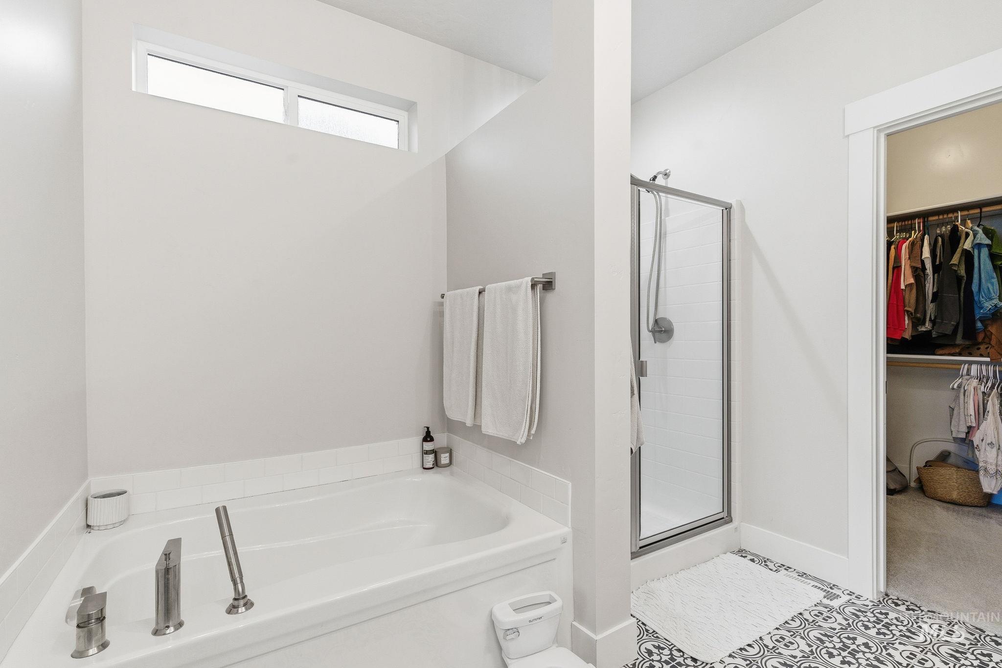Full bathroom featuring a walk in closet, a garden tub, a shower stall, and tile patterned floors