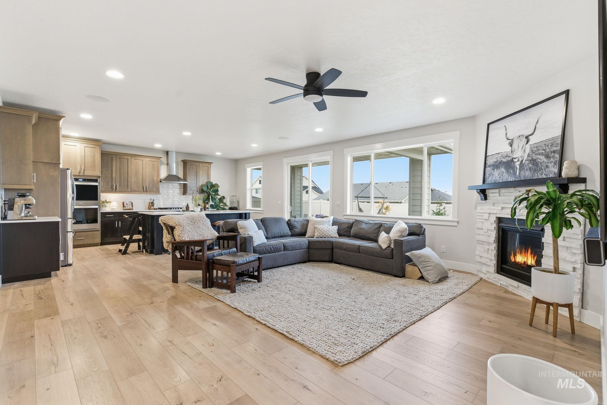 Living area with light wood finished floors, recessed lighting, ceiling fan, and a stone fireplace
